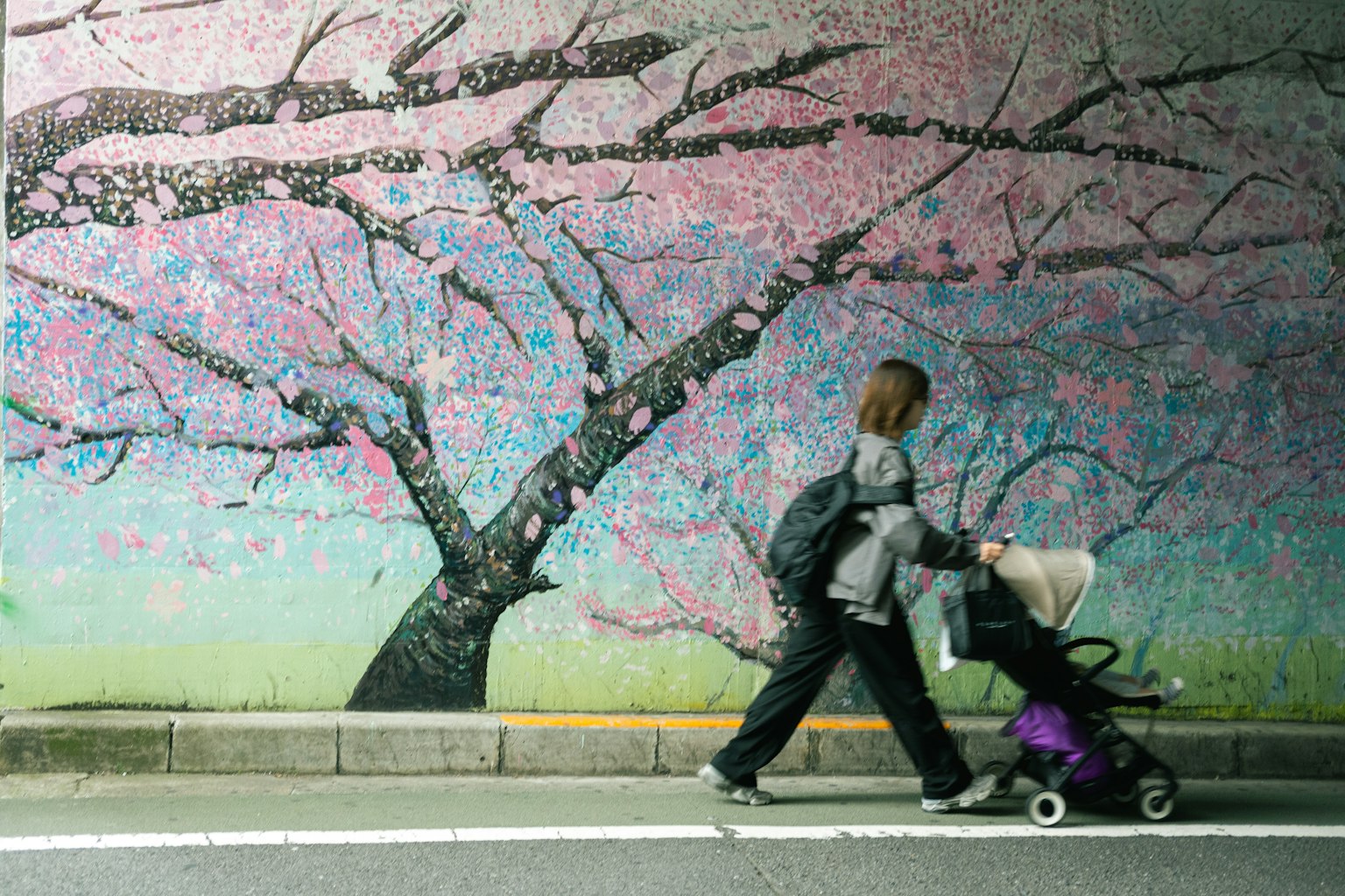 Una persona che cammina con un passeggino davanti a un murale di ciliegi in fiore