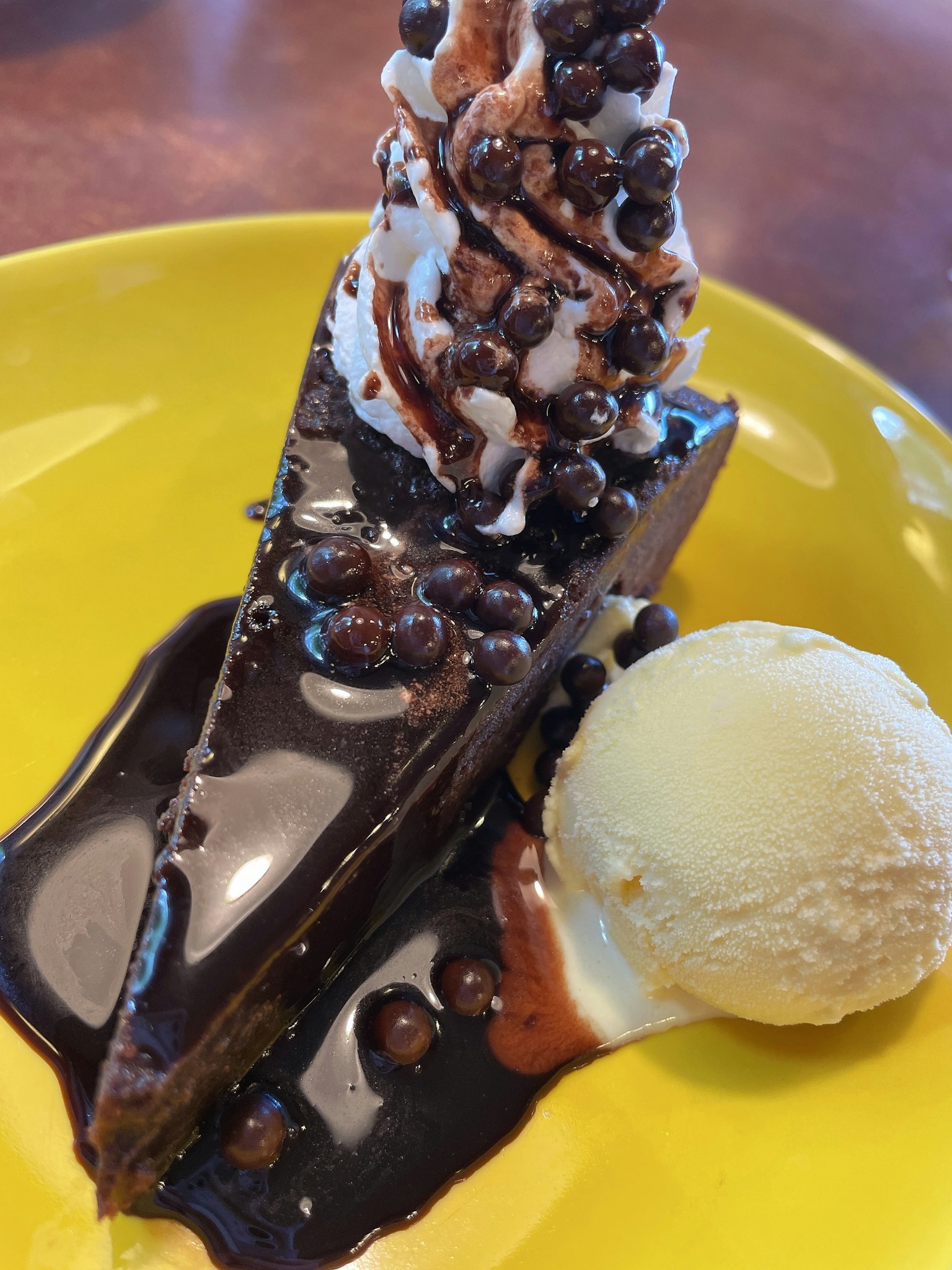 Une tranche de gâteau au chocolat garnie de crème fouettée et de pépites de chocolat servie avec une boule de glace à la vanille sur une assiette jaune