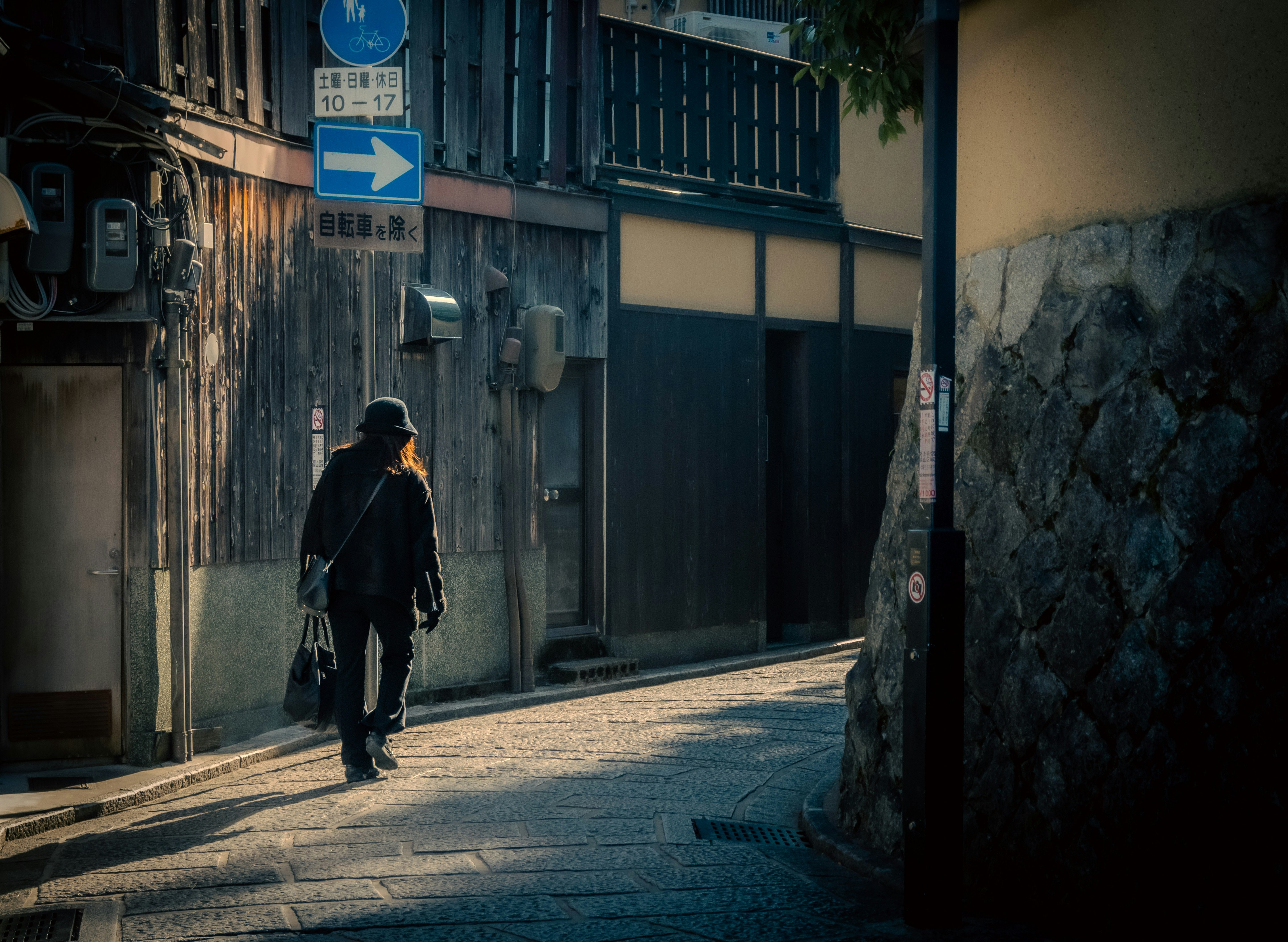 eine Person geht eine enge Gasse entlang mit blauen Straßenschildern und Ladenfassaden