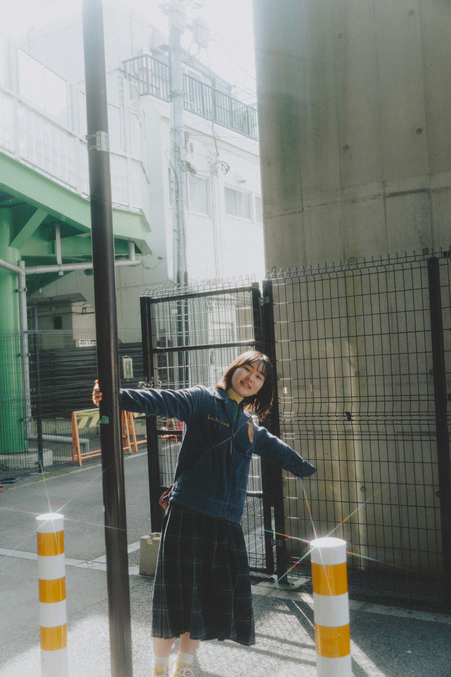 A woman in a blue sweater and black skirt joyfully spreading her arms in front of a pole