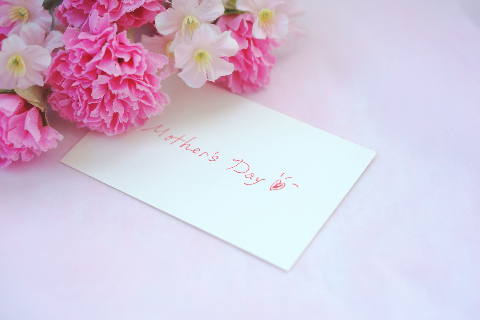 Una scena bella con fiori rosa e una carta bianca con un messaggio per la festa della mamma