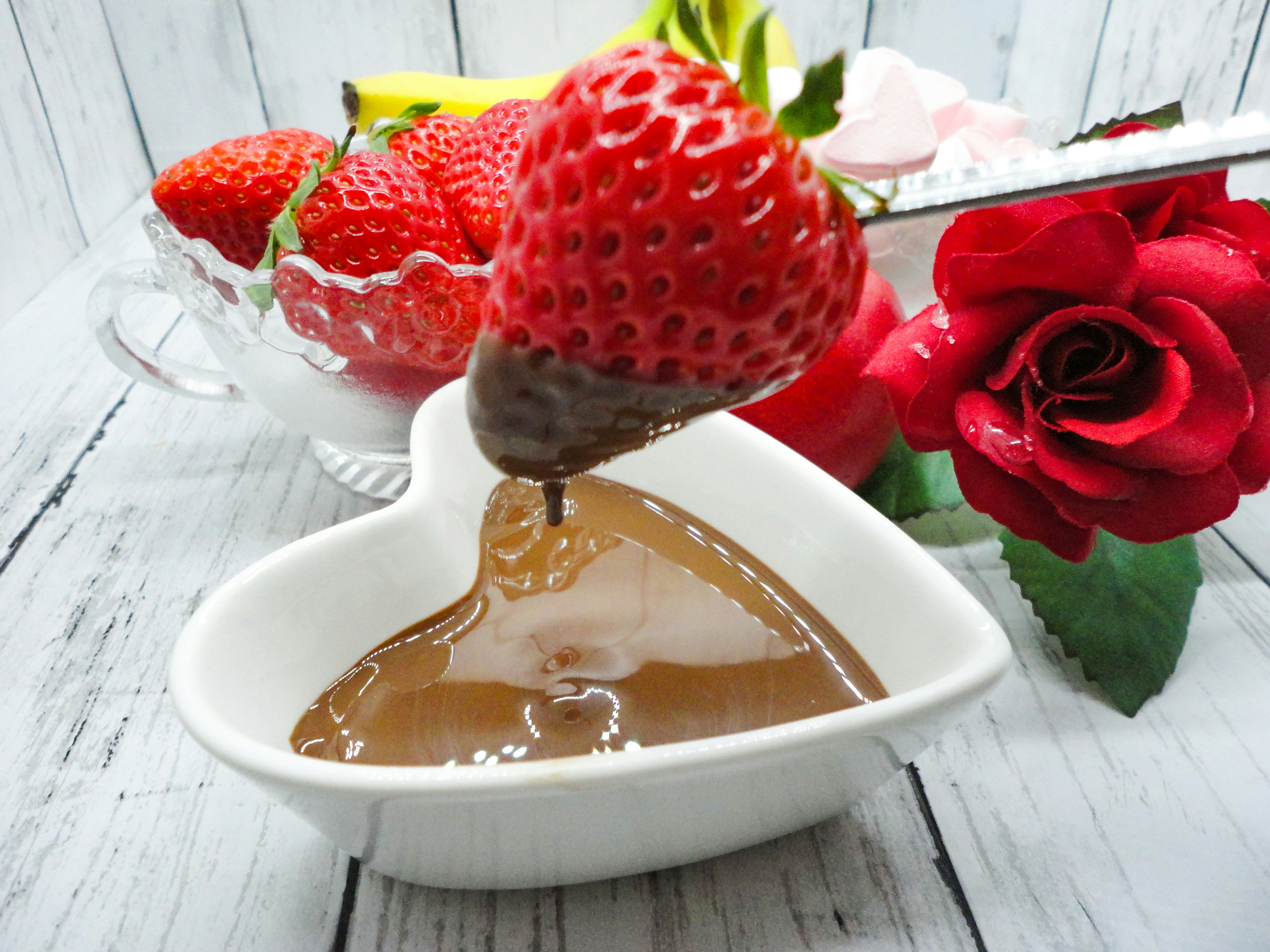 Schokoladensoße wird in eine weiße Schüssel gegossen mit Erdbeeren und Rosen-Deko