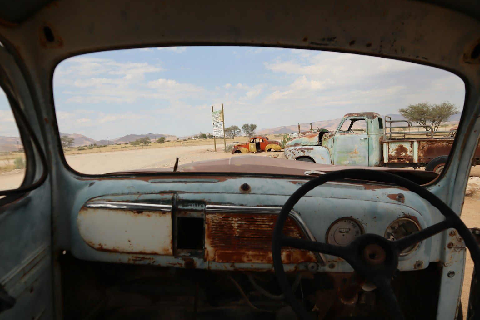 老式卡车驾驶座的视角 生锈的方向盘和仪表板 眼前的荒地和其他卡车