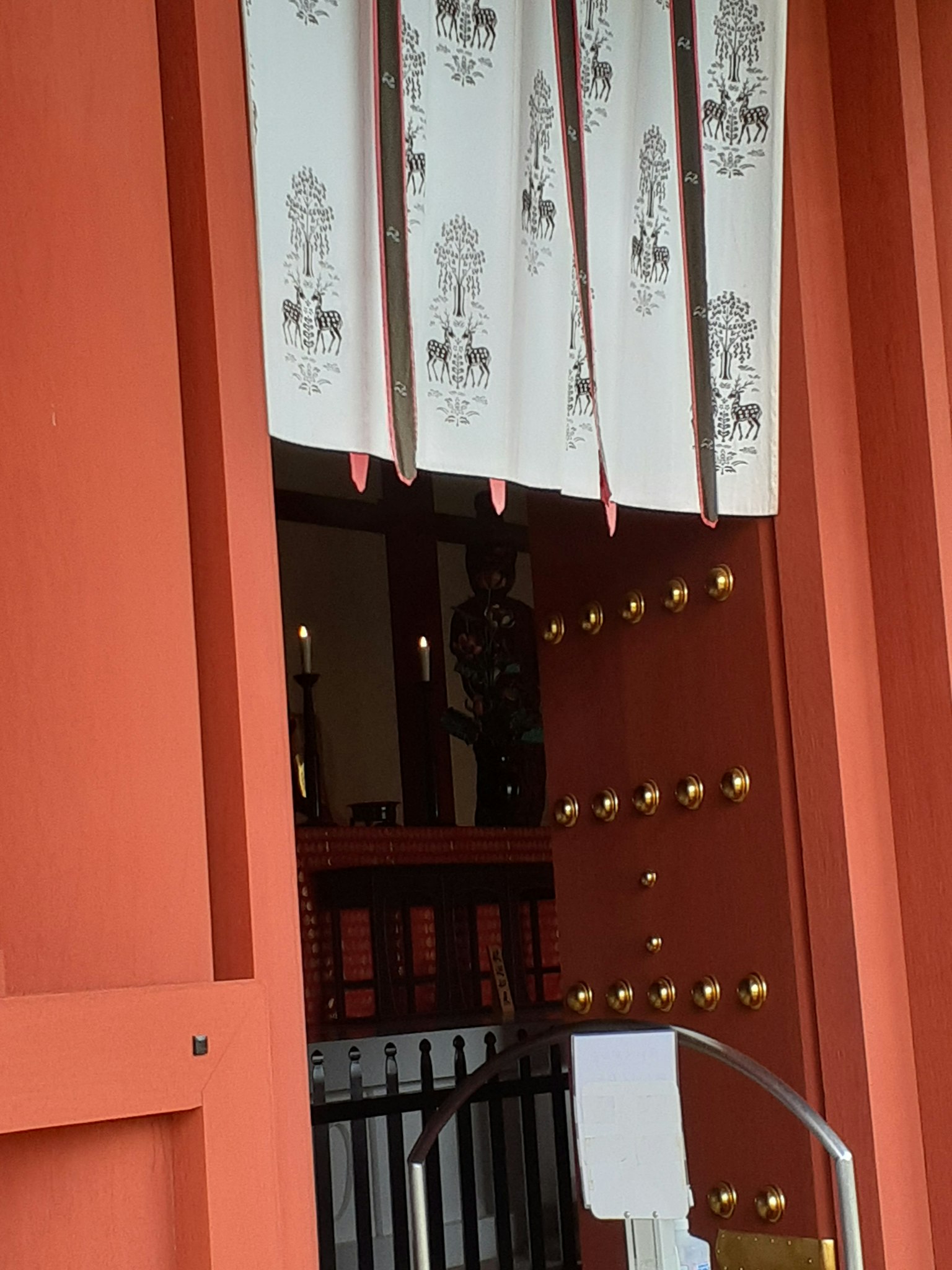 Foto di un'entrata di un santuario con porta in legno rosso e tende noren bianche