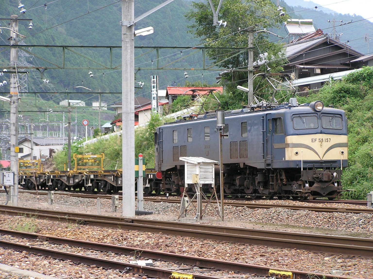 Kereta barang berhenti di stasiun kereta dengan latar belakang gunung hijau