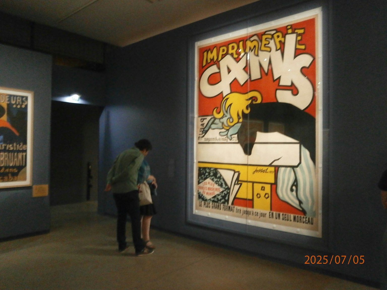 Ein Elternteil und ein Kind betrachten ein großes Plakat in einem Ausstellungsraum Das Plakat zeigt ein gedrucktes Karnevaldesign