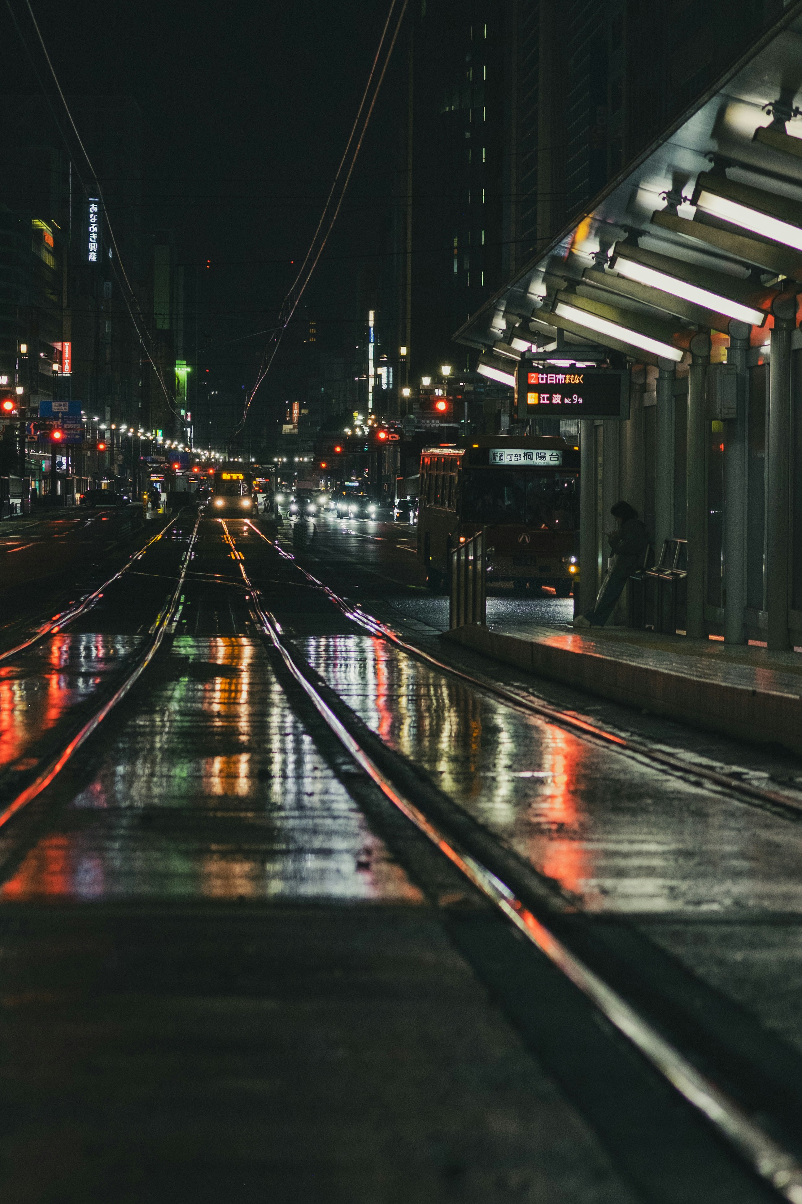 Nächtliche Stadtstraße mit Spiegelungen auf nasser Fahrbahn entlang eines erhöhten Gehwegs