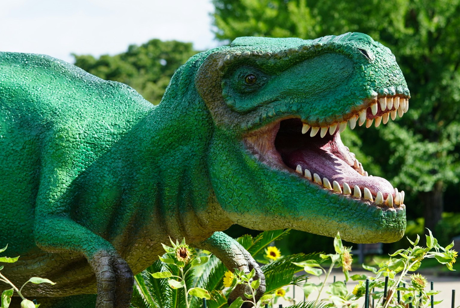 Modello di dinosauro verde posizionato tra le piante