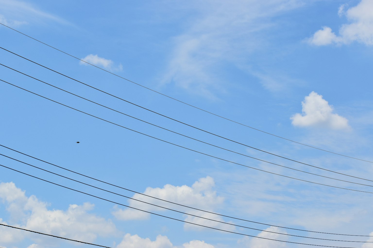 Langit biru dengan awan putih dan saluran listrik membentang di seluruh pemandangan