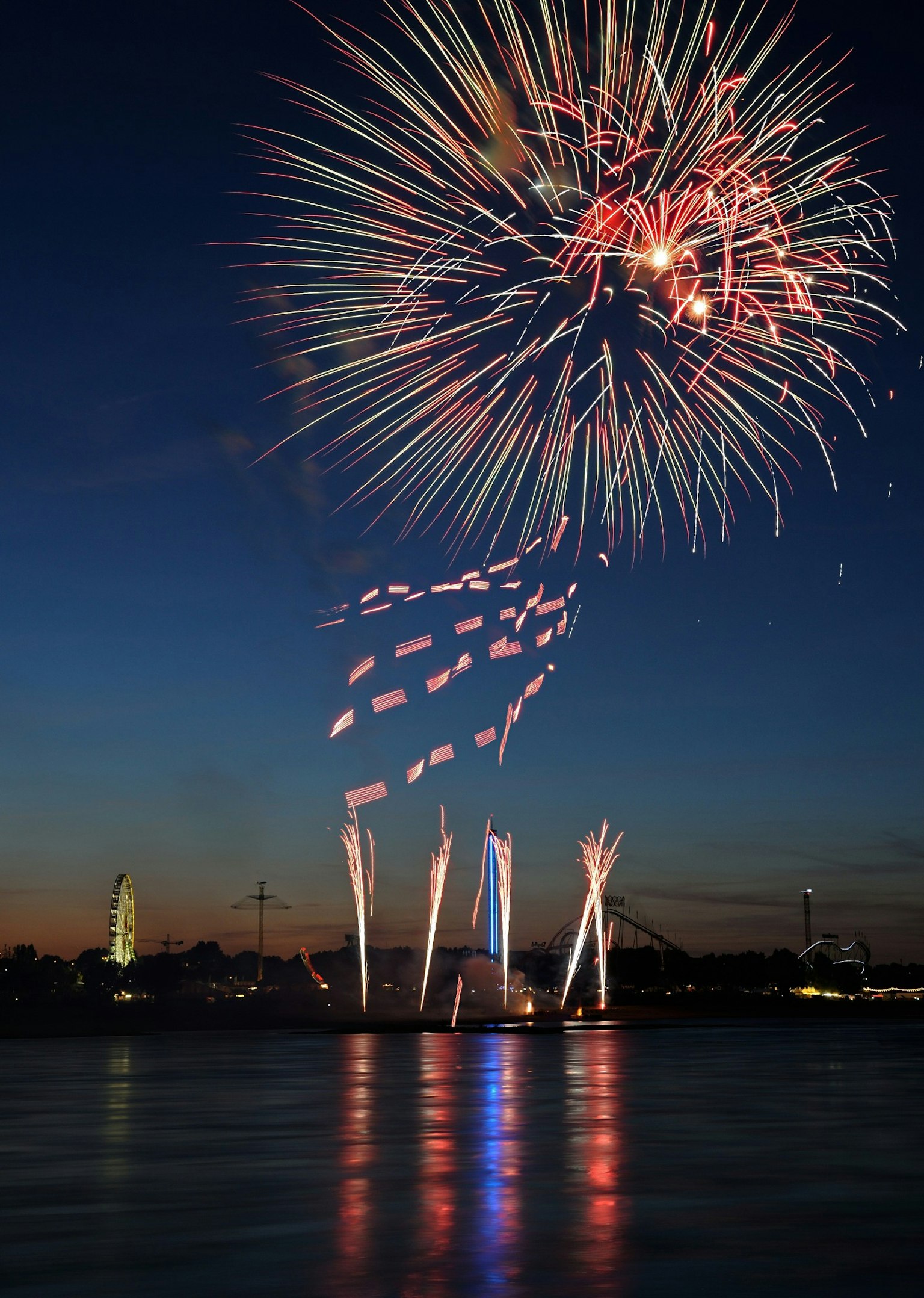 Buntes Feuerwerk über einem ruhigen Gewässer bei Dämmerung