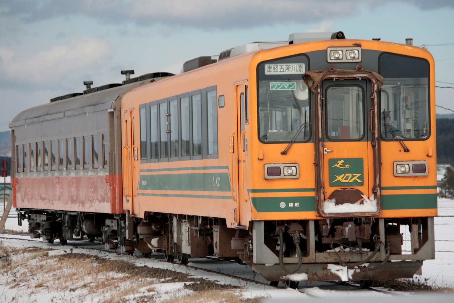 Un treno arancione con un vagone passeggeri rosso che corre su binari coperti di neve
