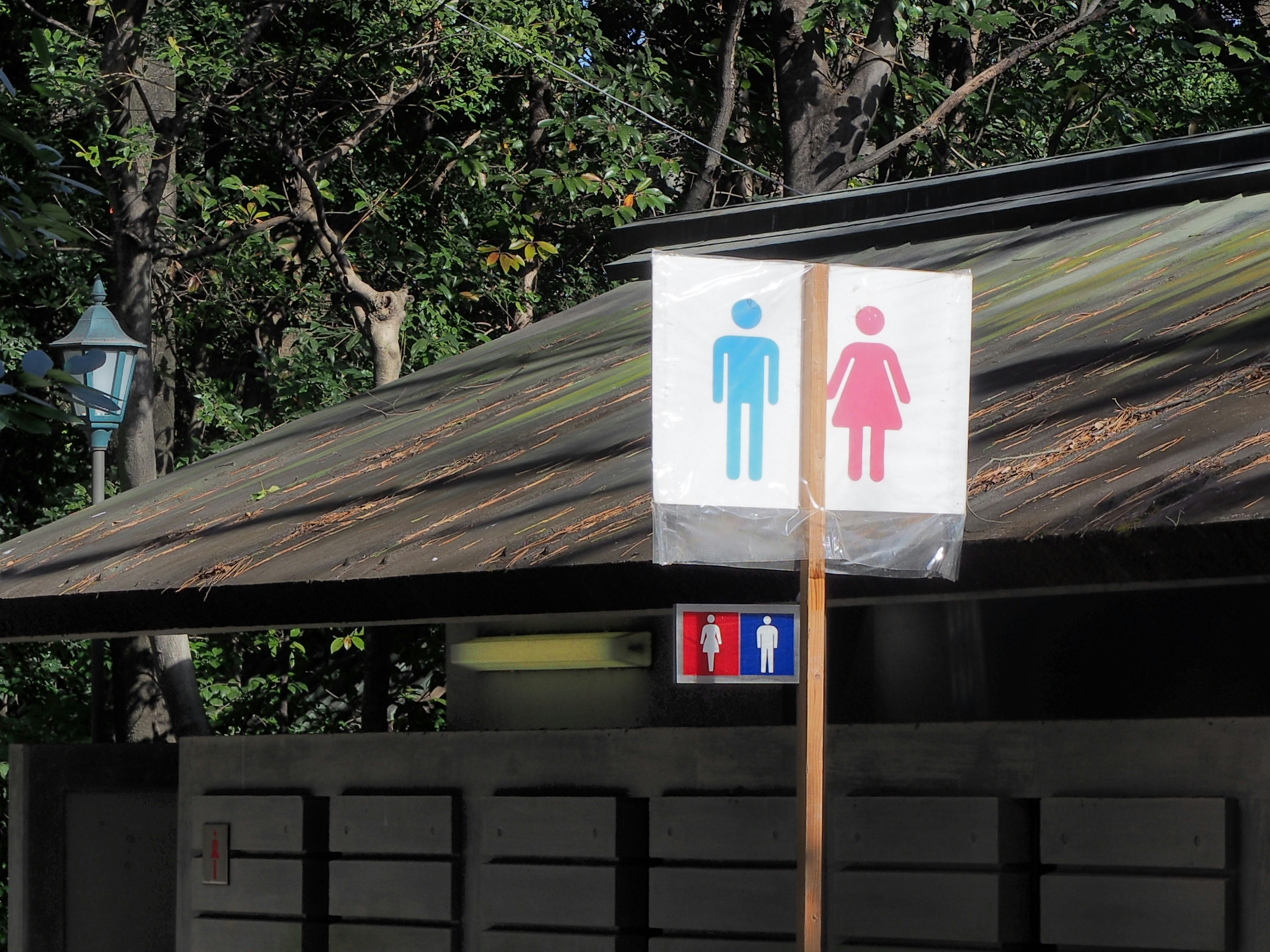 outdoor restroom wayfinding sign at an entrance surrounded by trees