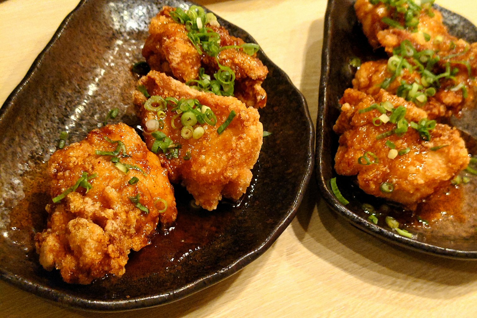 Crispy chicken pieces garnished with green onions on black plates