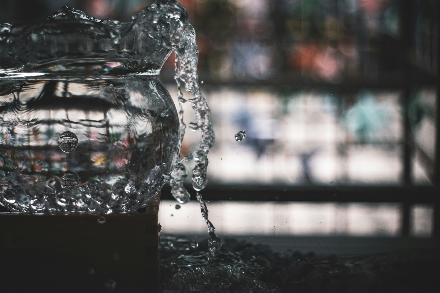 Close-up of a glass fishbowl with water spilling out blurred colorful background