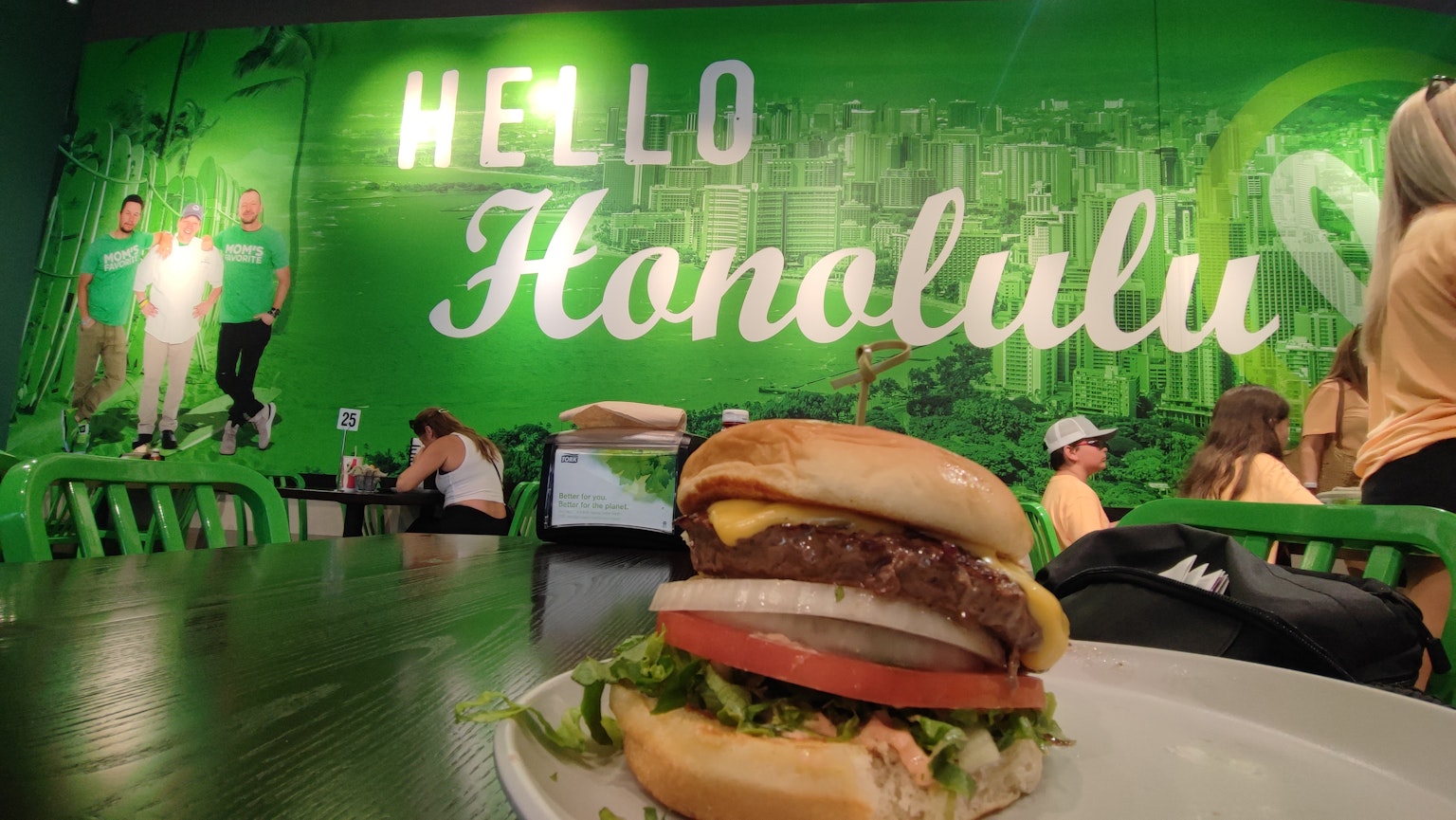 Un hamburger devant un mur vert avec le texte Bonjour Honolulu dans un café