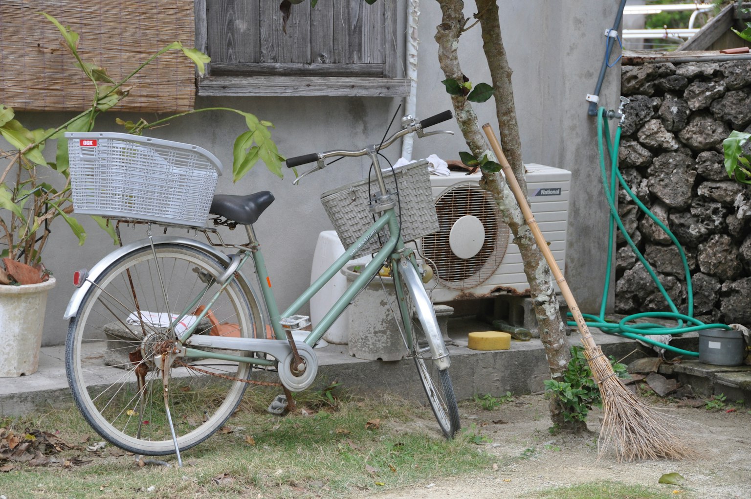Sepeda hijau diparkir di luar dengan AC dan tanaman di latar belakang