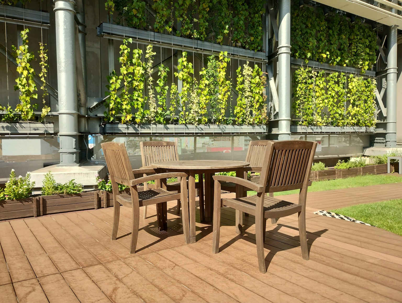 Holztisch und Stuhlset auf einer Terrasse mit einer grünen Wand im Hintergrund