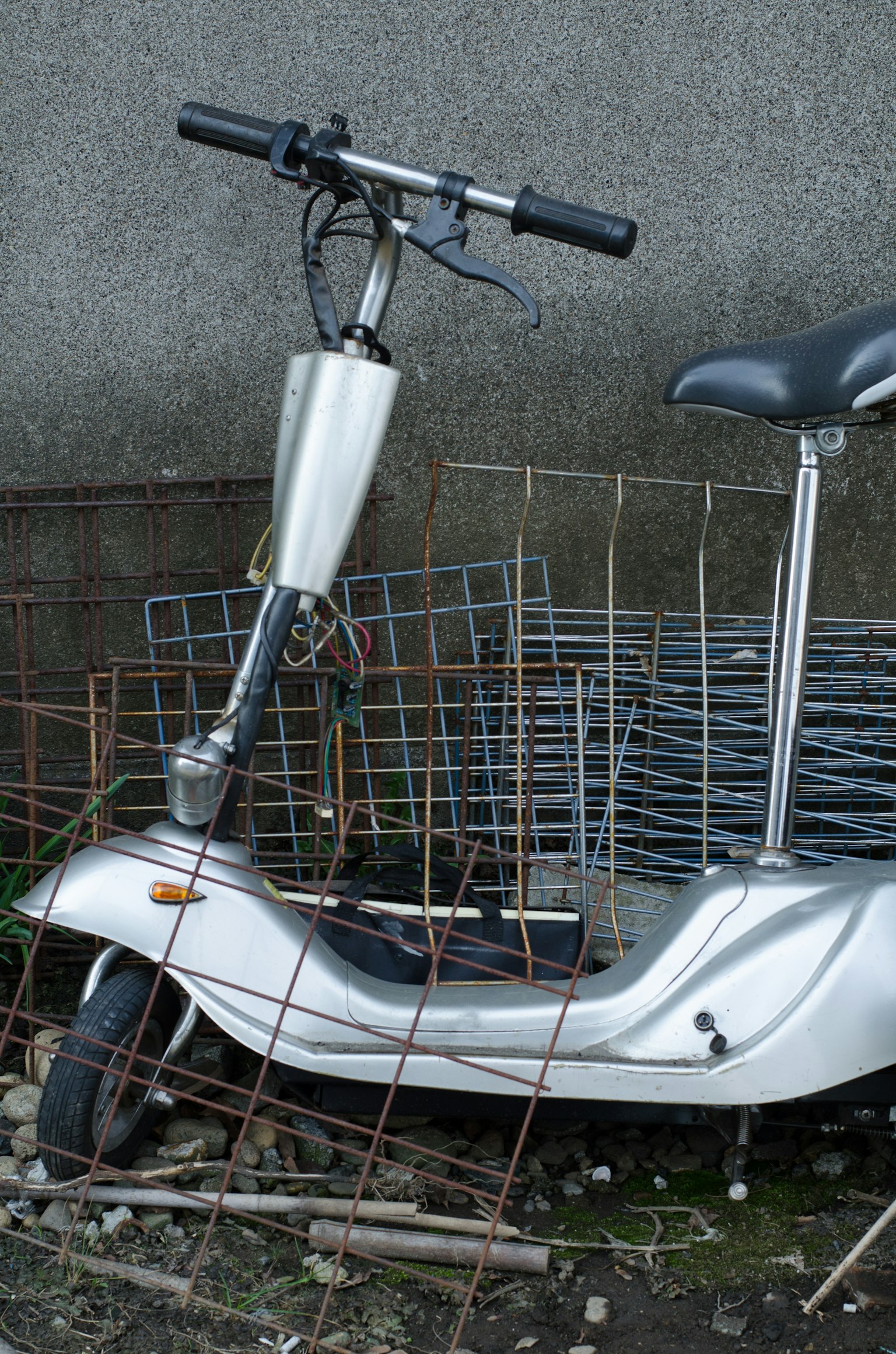 Scooter eléctrico plateado rodeado de rejillas metálicas