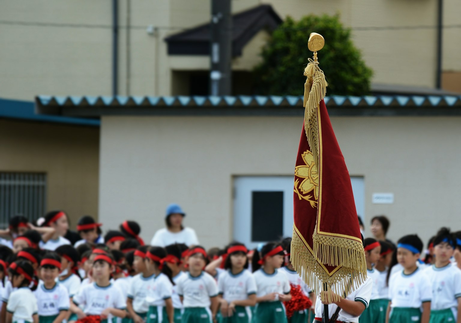 運動會上孩子們聚集在一起舉著旗幟，背景是學校建築