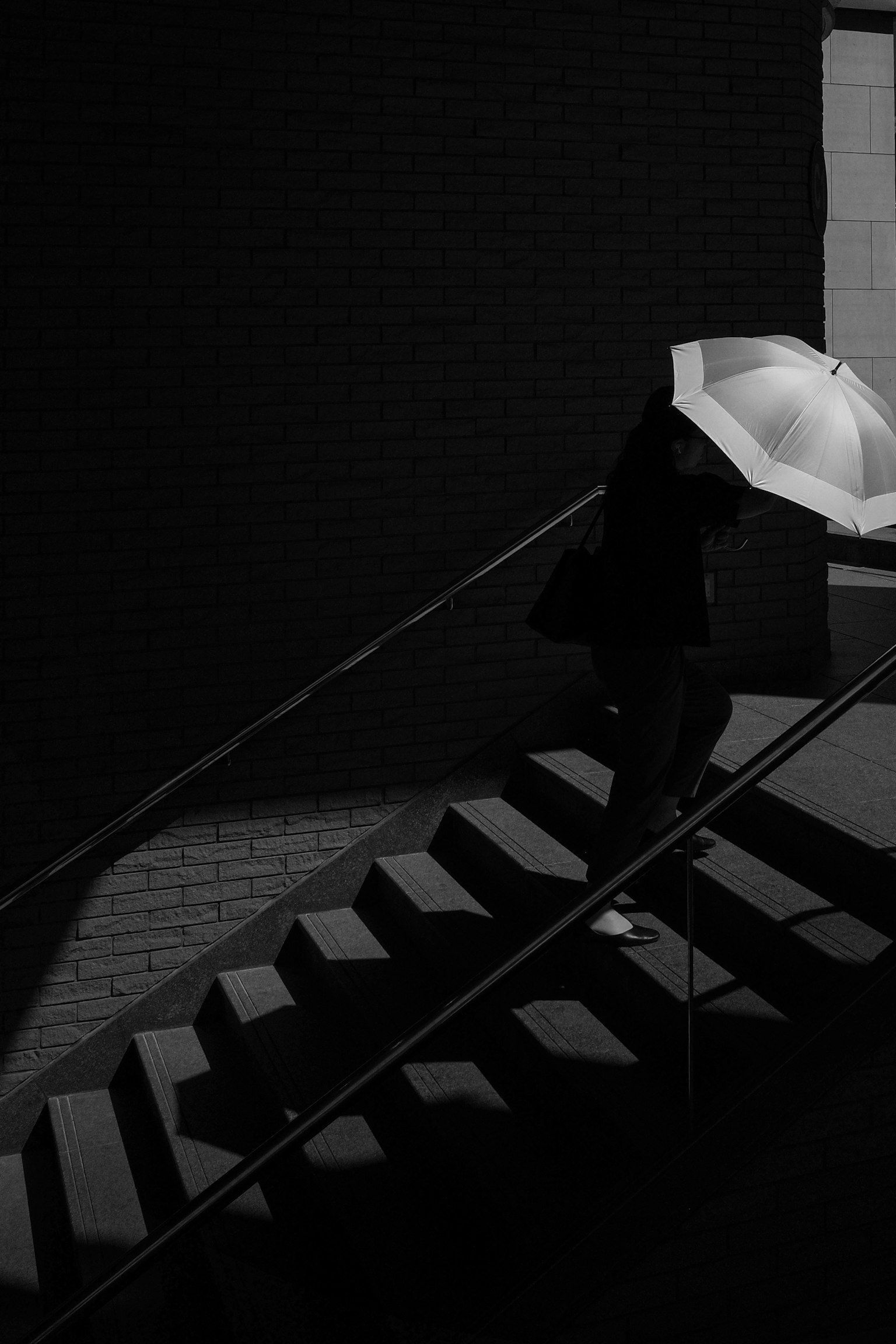 Foto in bianco e nero di una persona che sale le scale con un ombrello
