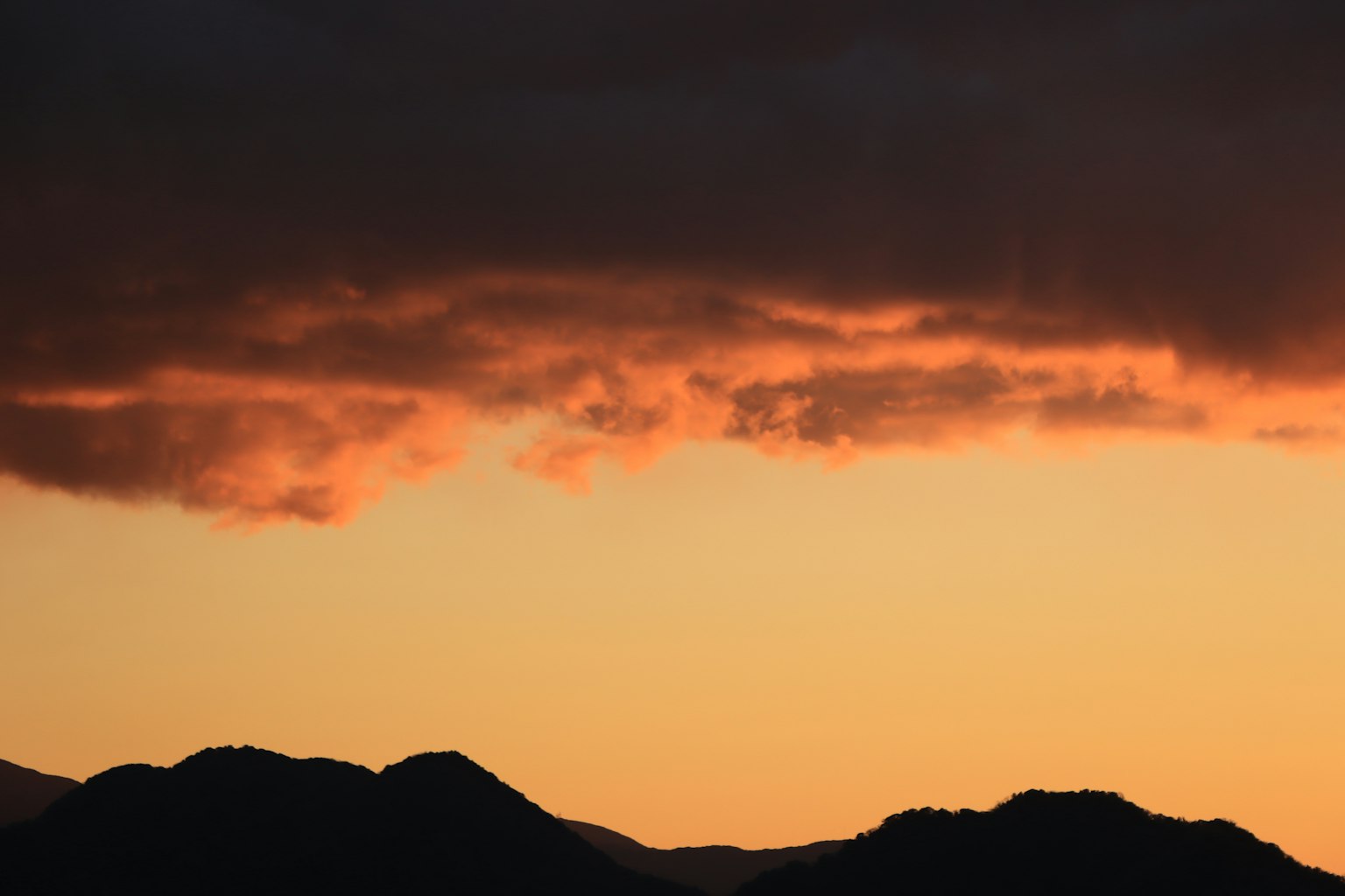 Cielo anaranjado de atardecer con siluetas de montañas