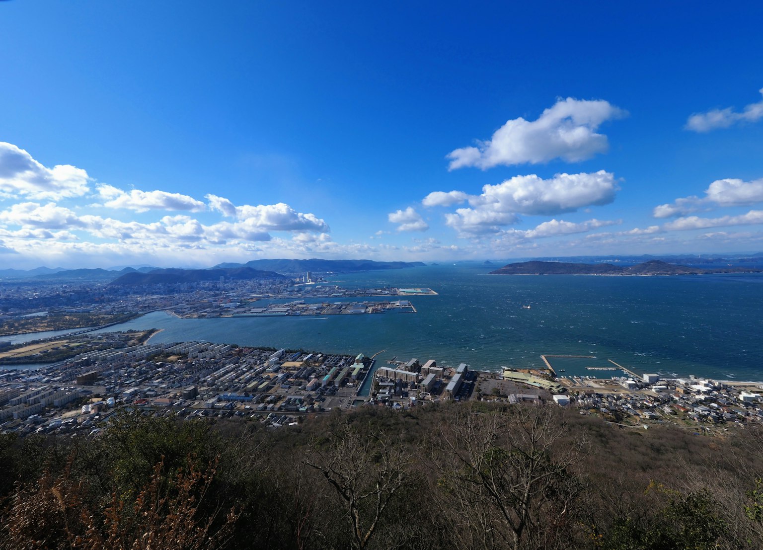 Vista costera pintoresca con cielo azul y nubes que muestra una ciudad portuaria y montañas