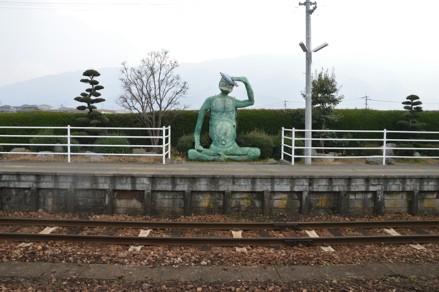 A green statue sitting beside the railway tracks at a train station