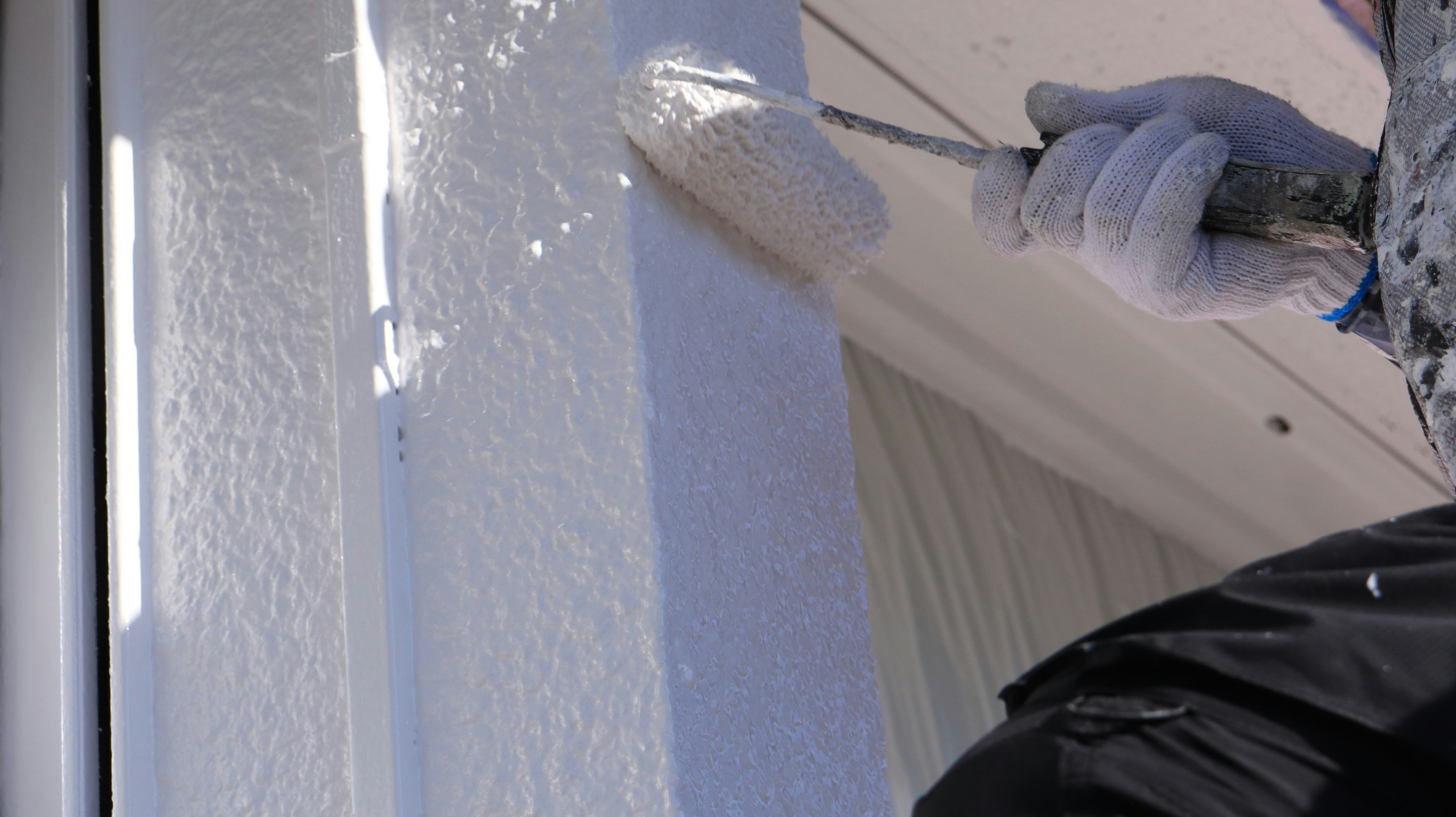 hands painting a white wall with a roller