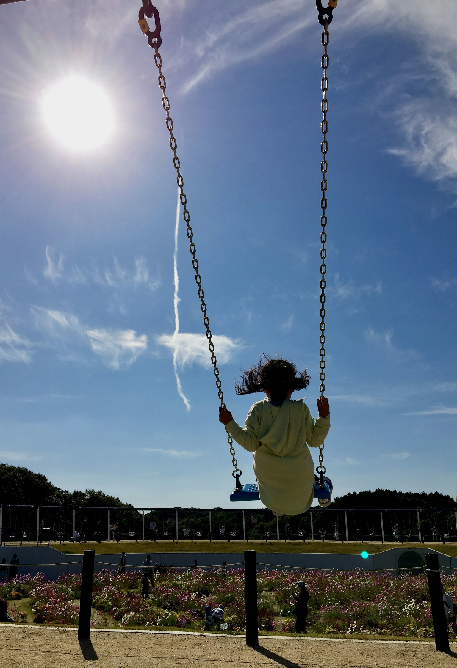 Enfant jouant sur une balançoire soleil brillant et ciel bleu fleurs colorées visibles