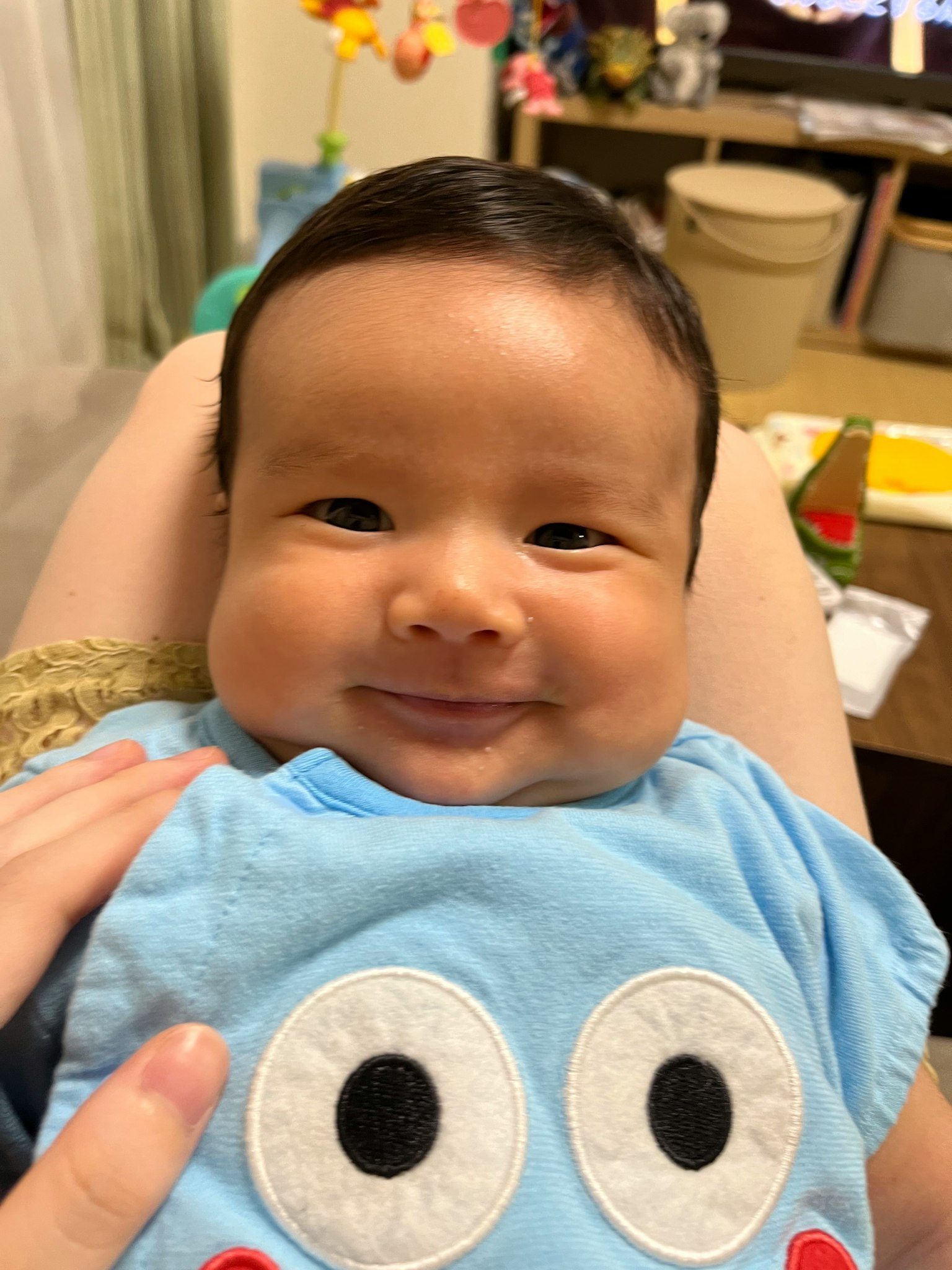 Un bébé souriant portant une chemise bleue avec des yeux de dessin animé regardant l'appareil photo