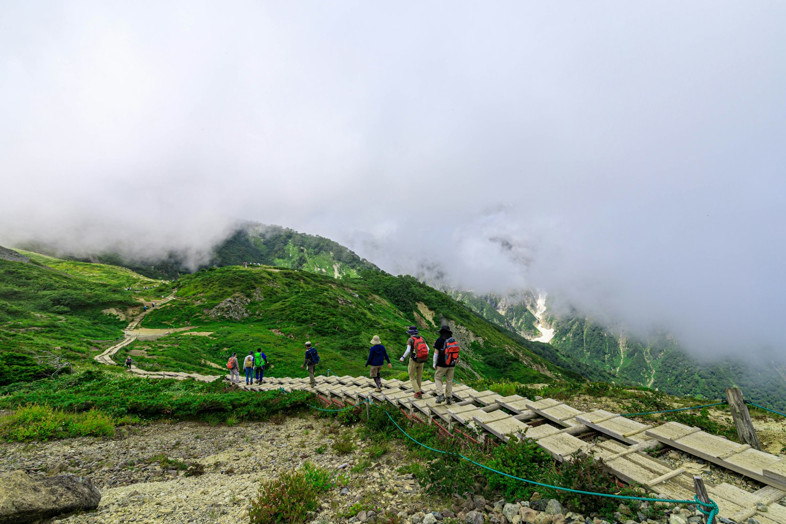 Pendaki berjalan di sepanjang jalur gunung hijau yang diselimuti kabut