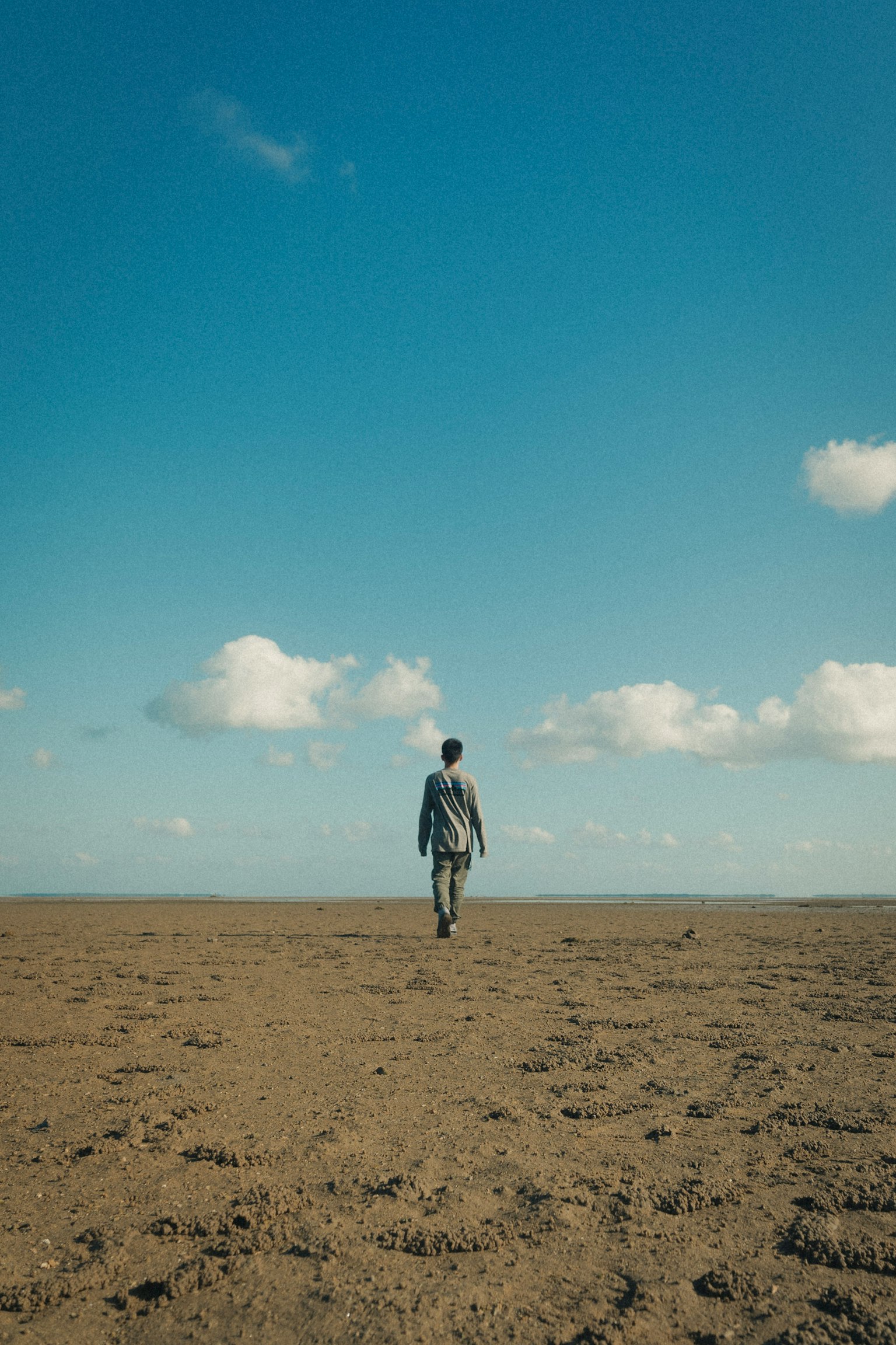Una persona caminando por un vasto paisaje arenoso bajo un cielo azul