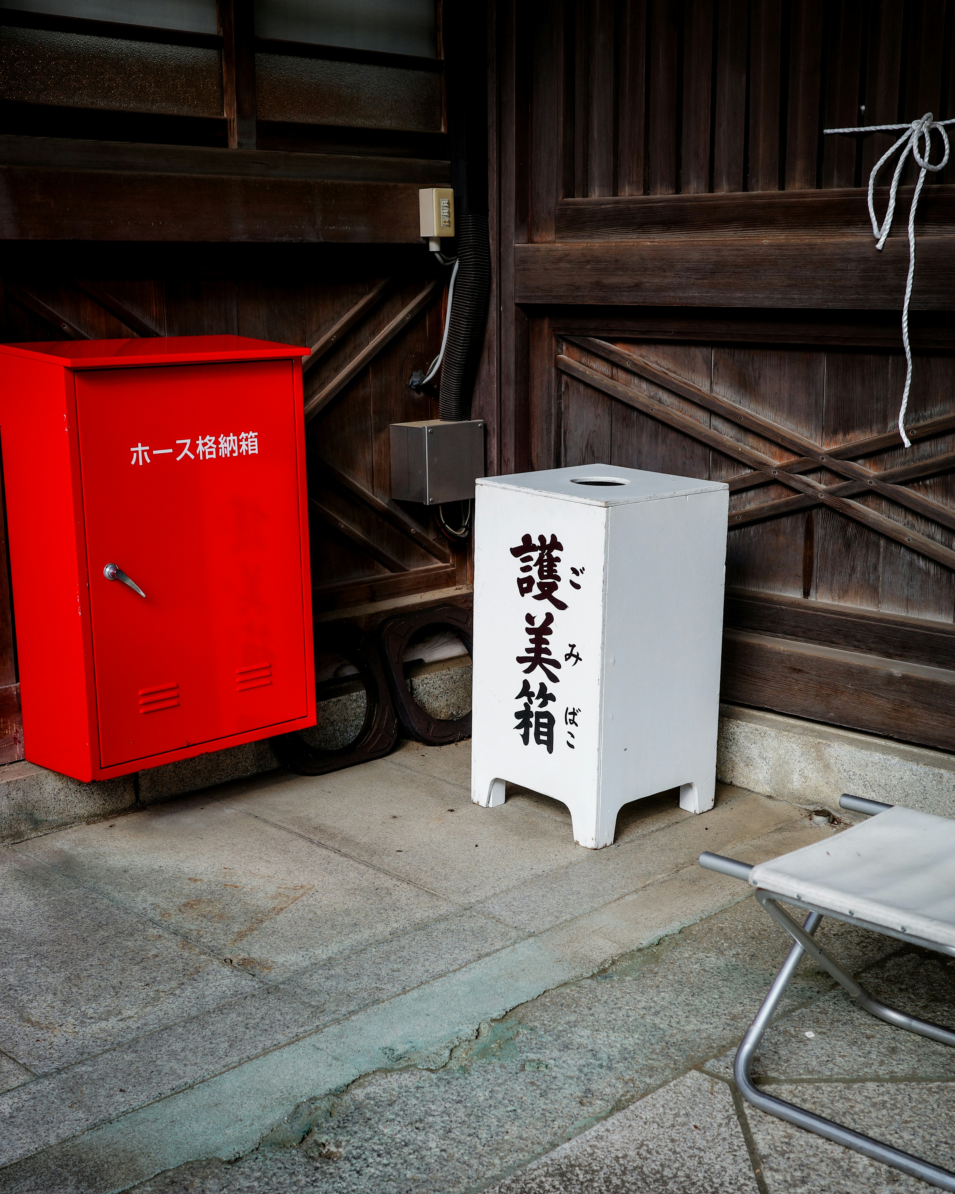 木造の軒先に置かれた赤い投函箱と白い小さな箱