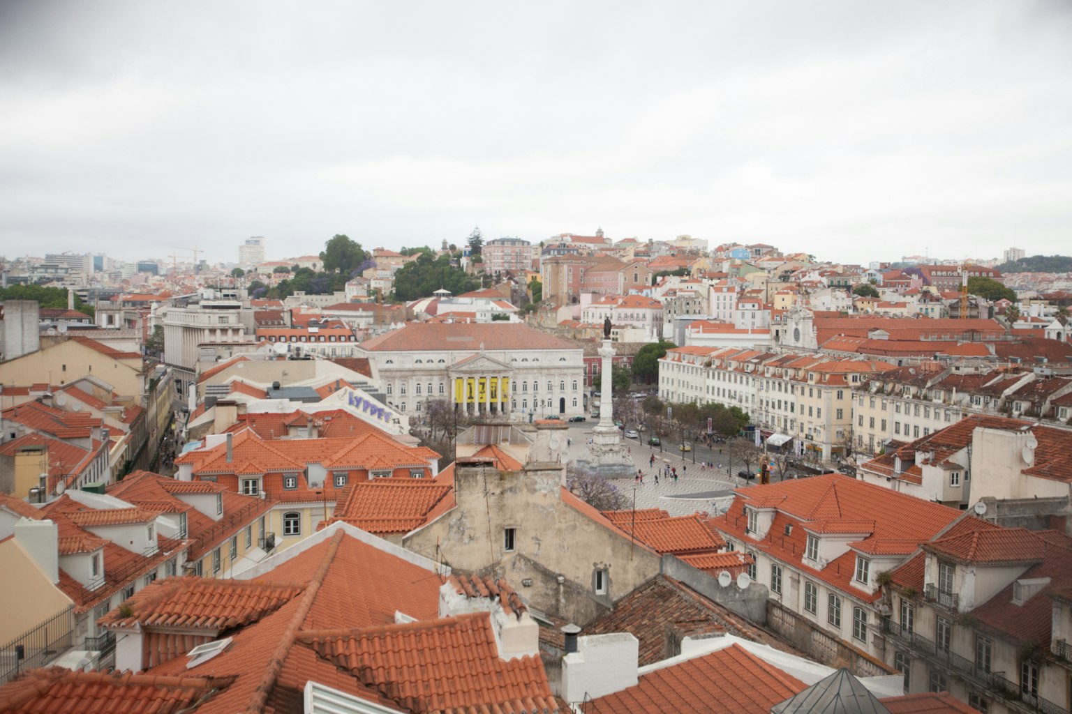 Lisbon rooftops with red tiles and a view of a square under a cloudy sky