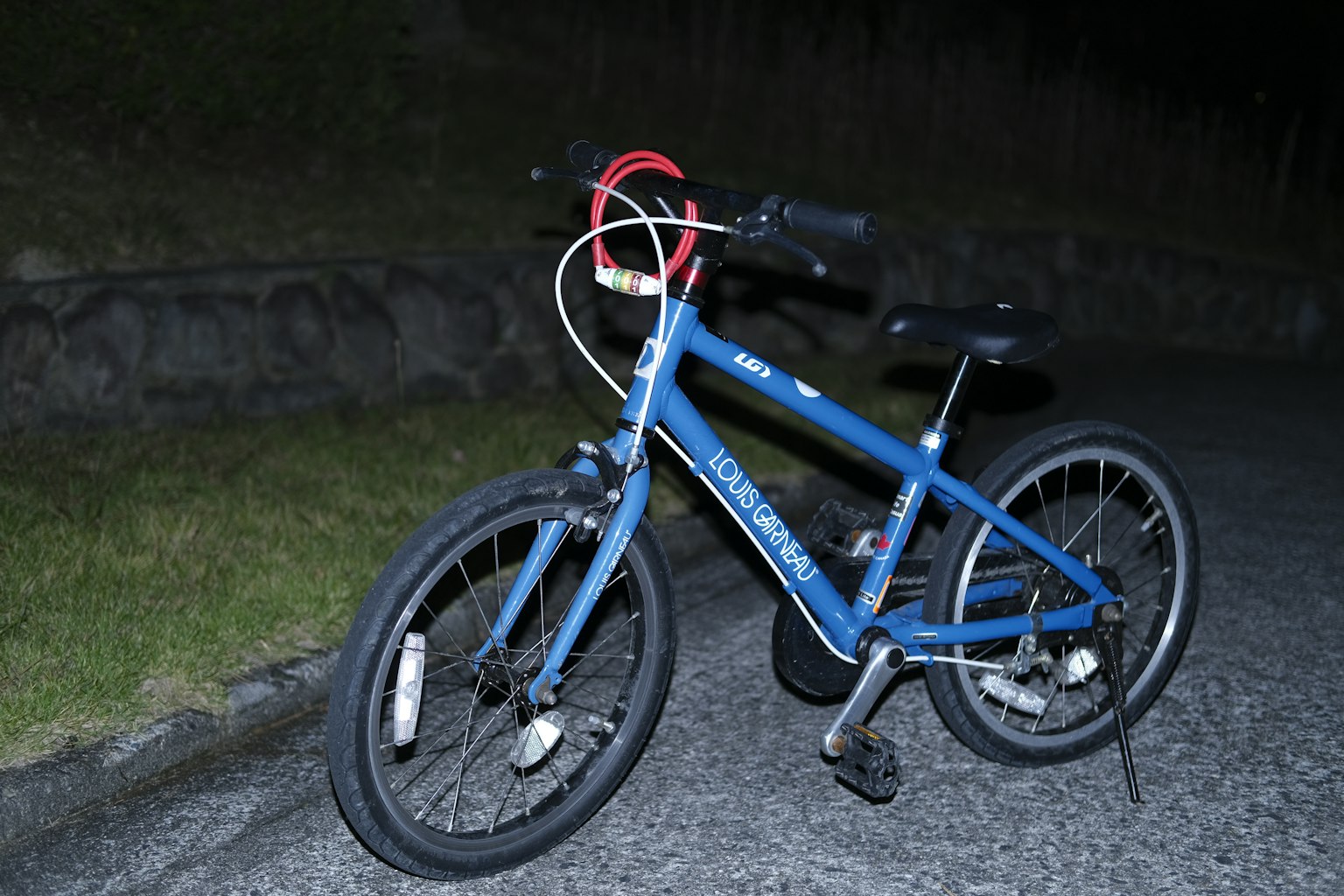 Una bicicletta blu parcheggiata su una strada notturna con ruote argentate e un manubrio rosso