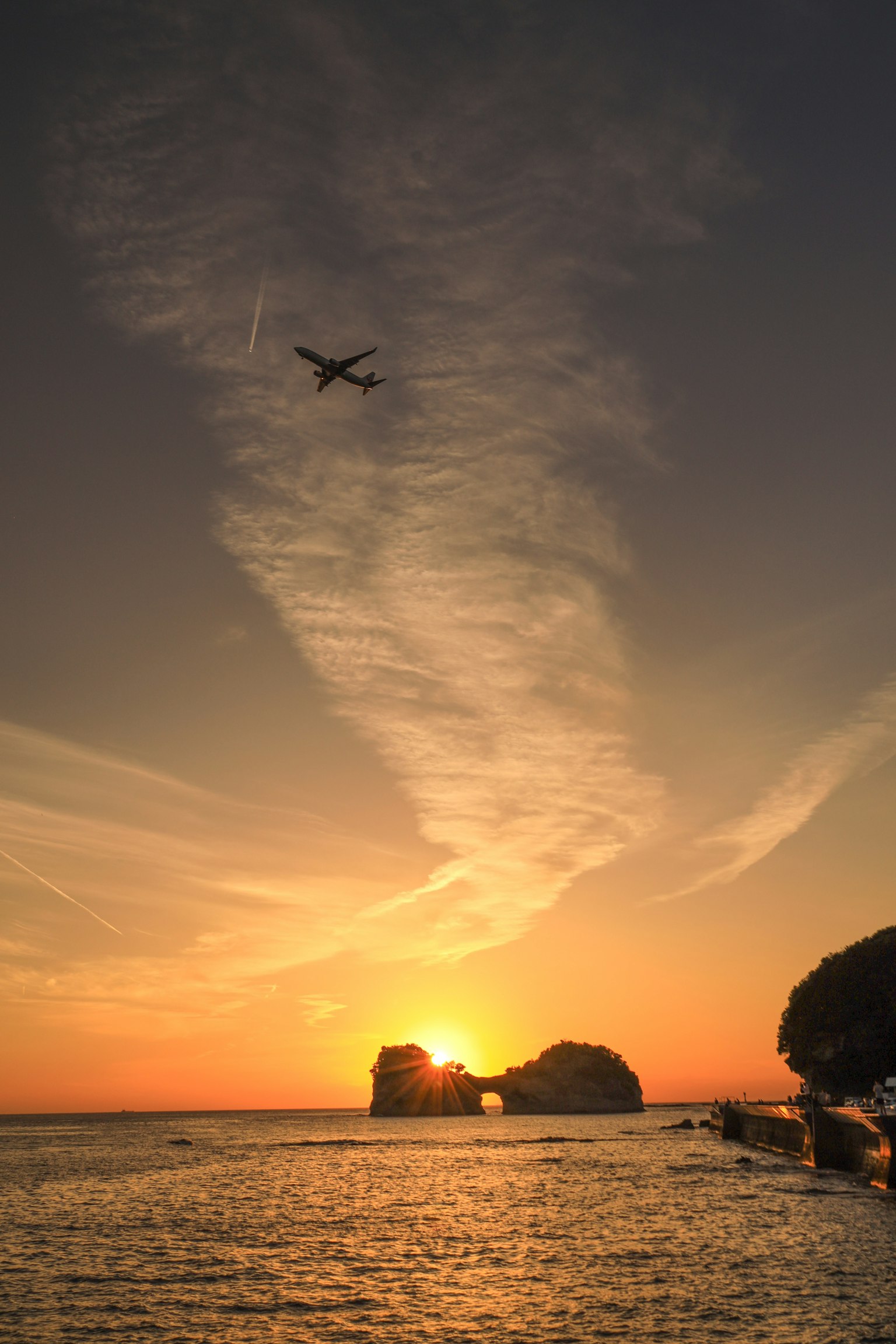 Un avión volando contra un atardecer sobre el océano con formaciones rocosas
