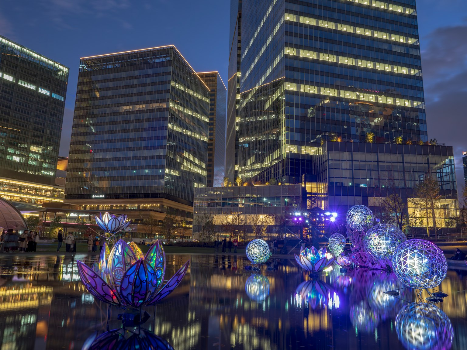 Gratte-ciels modernes se reflétant dans l'eau avec des orbes et des fleurs lumineuses la nuit