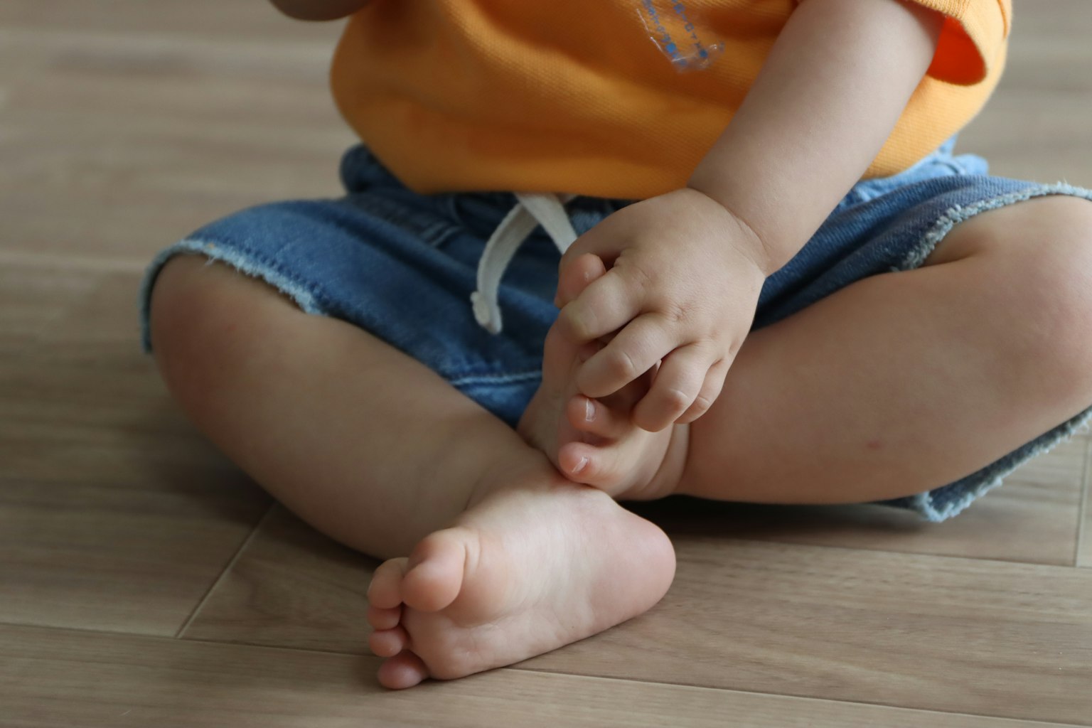 Un niño sentado con las piernas cruzadas vistiendo una camiseta naranja y pantalones cortos de mezclilla