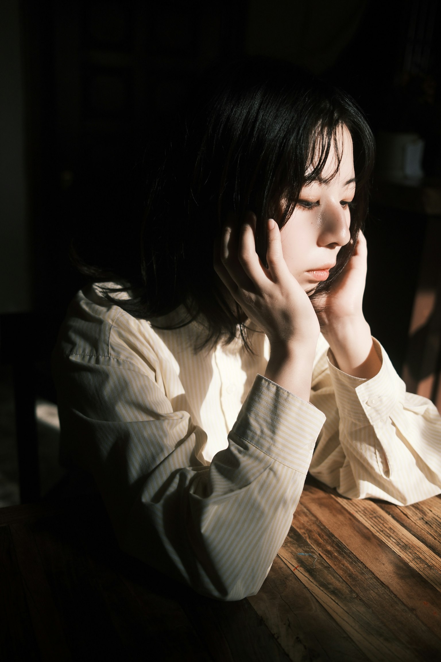 女性が手を顔に当てて考え込んでいる姿 明るい光と影が印象的