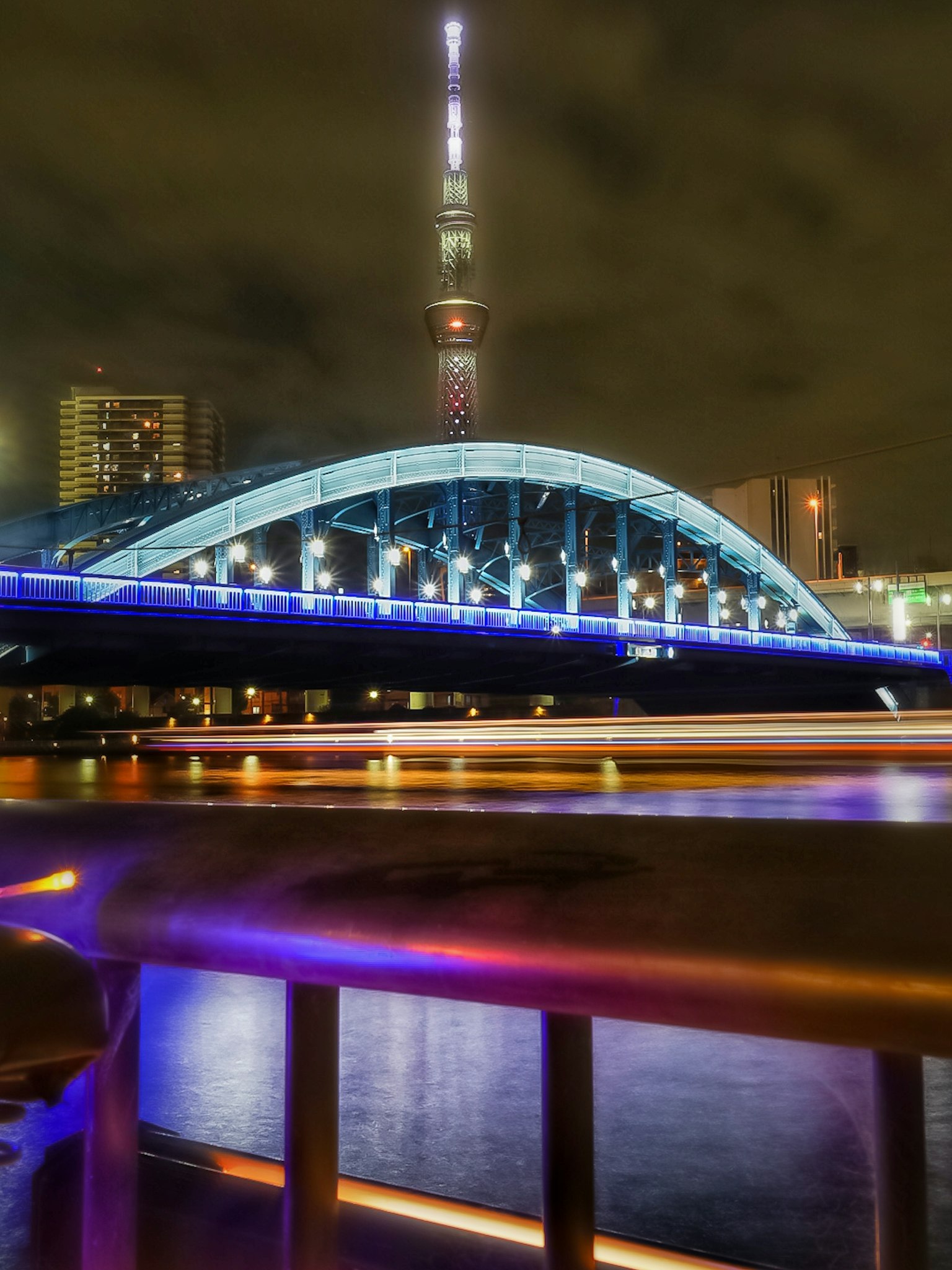 Nachtansicht einer Brücke mit der Tokyo Skytree im Hintergrund, beleuchtet in Blau und Lila