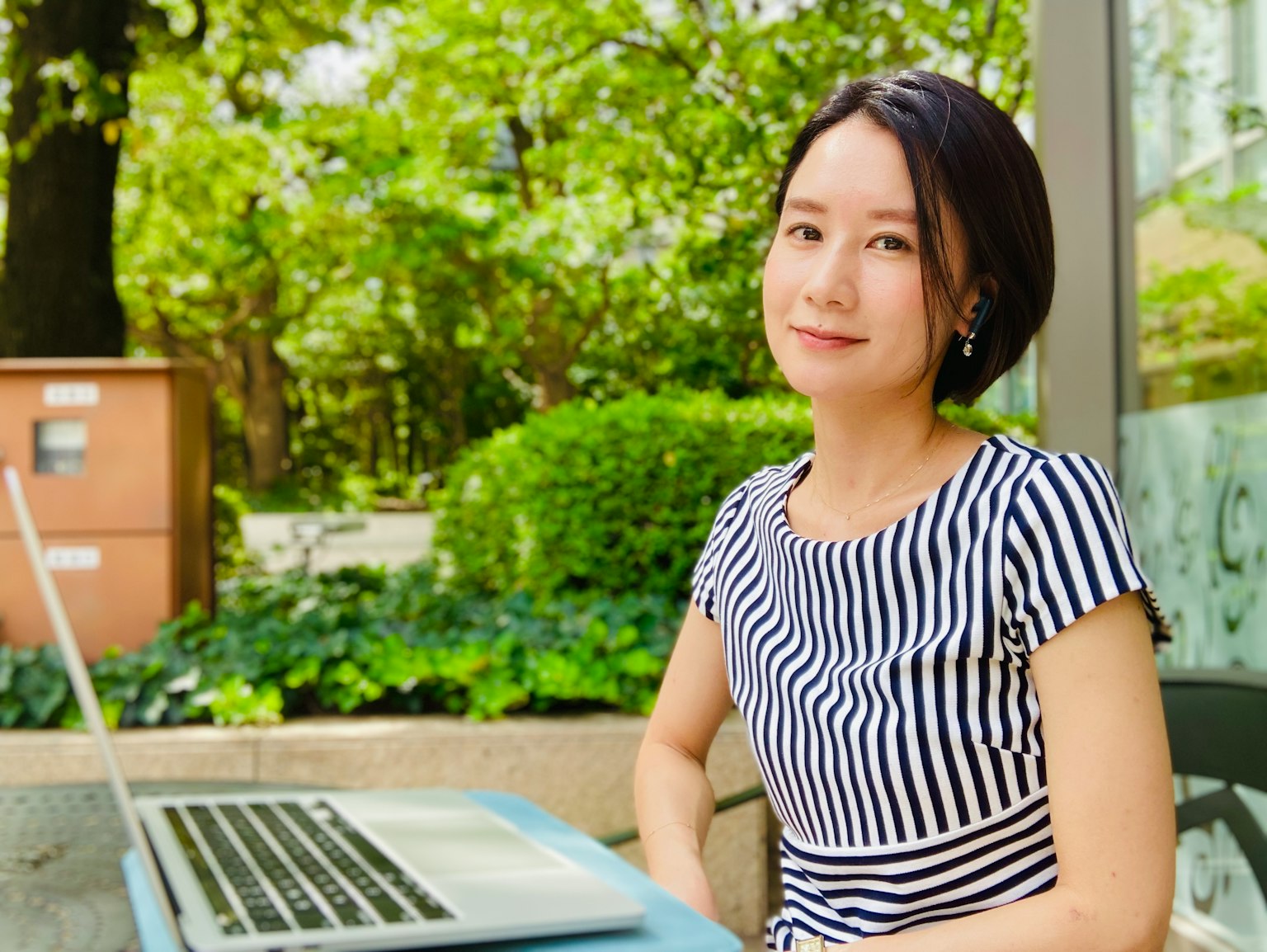 스트라이프 드레스를 입은 여성이 노트북 앞에 앉아 있으며 푸른 배경이 있다