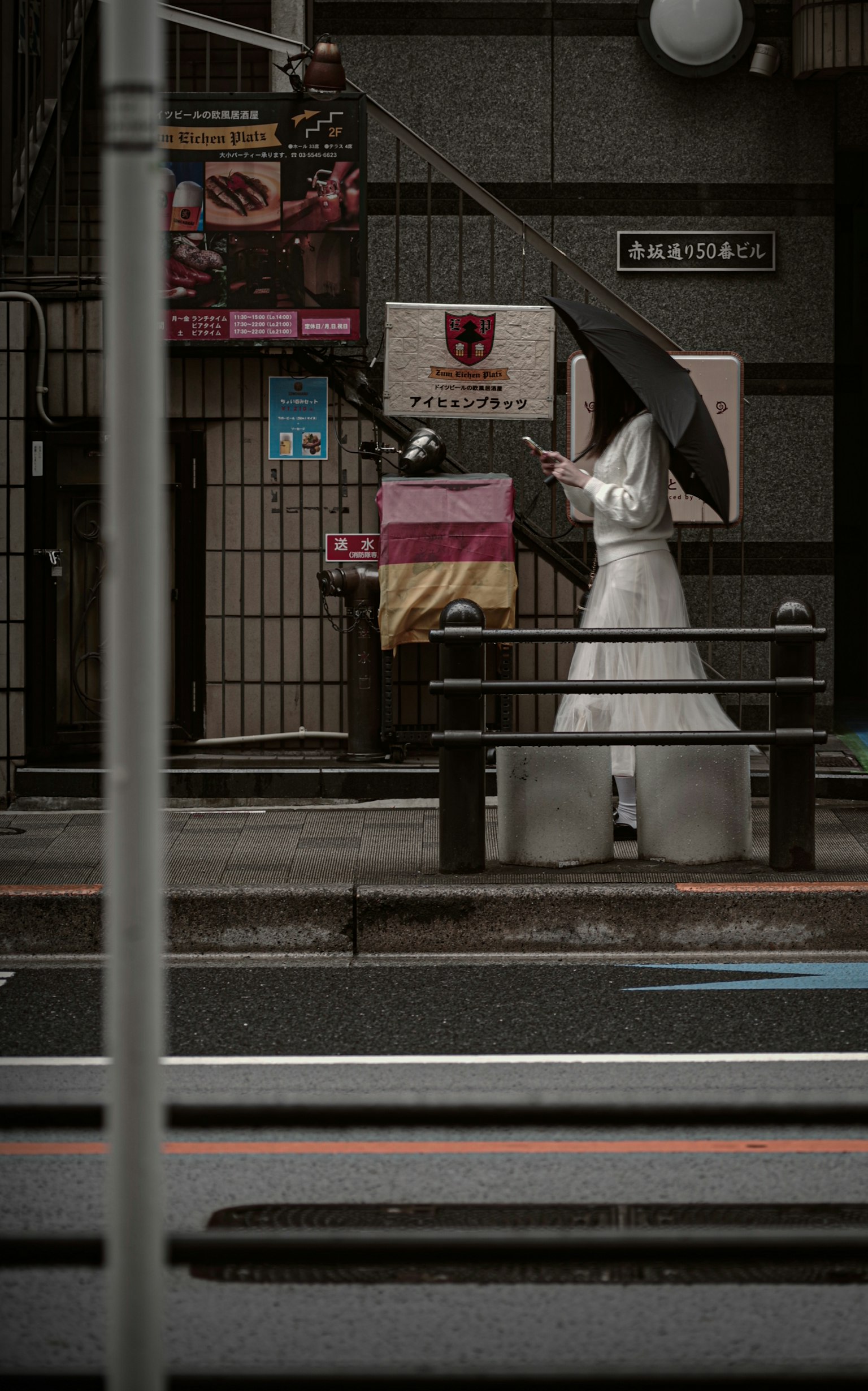 A person in a white outfit holding an umbrella stands on a city street