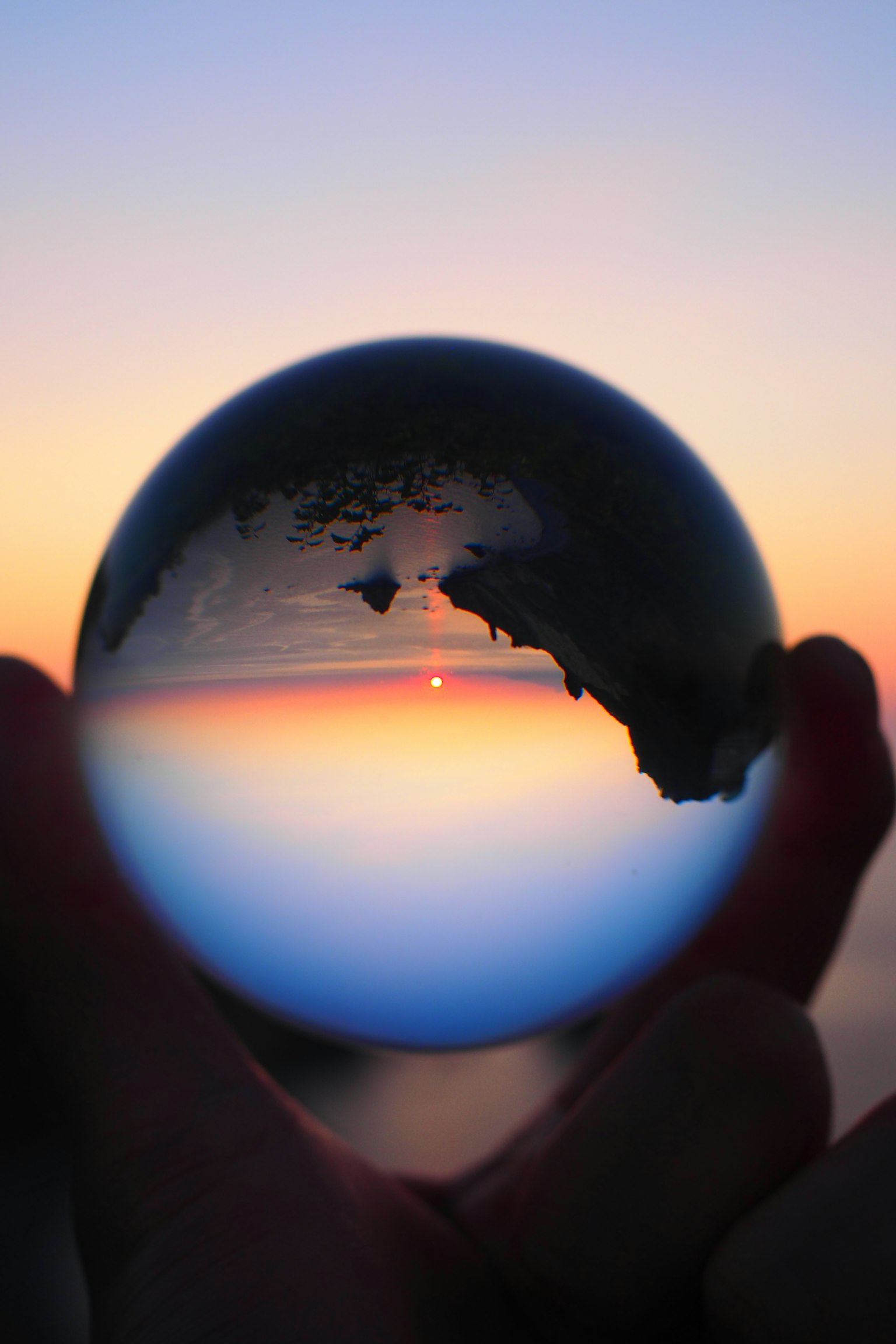 Silueta de una mano sosteniendo una bola de cristal que refleja un atardecer