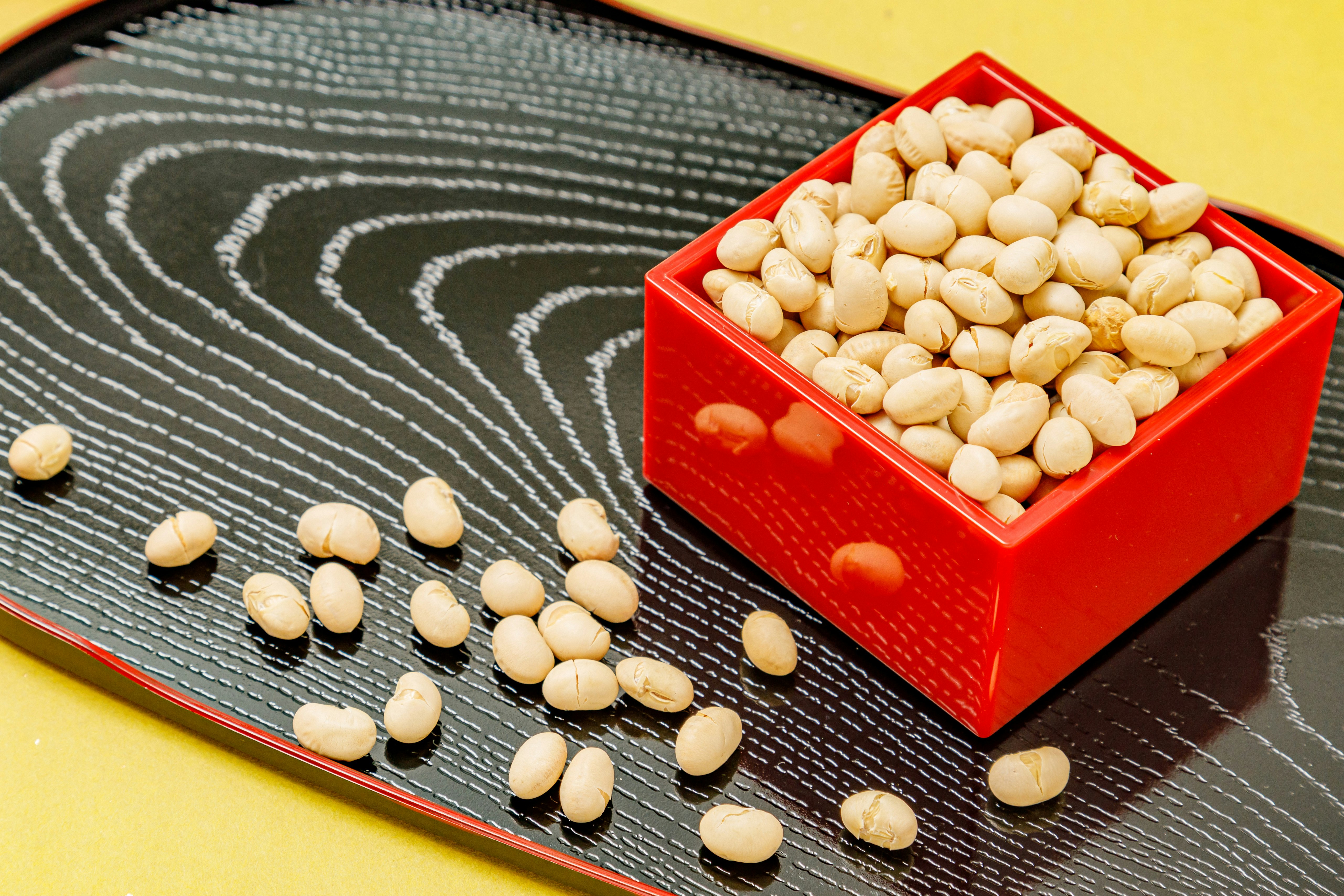 節分の福豆（大豆）を盛った赤い器と豆の散らばる皿