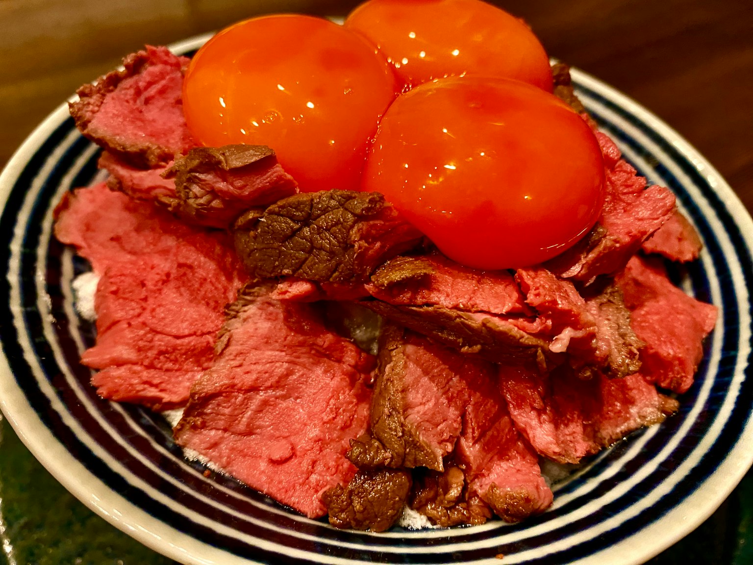 A dish featuring thin slices of beef topped with three egg yolks