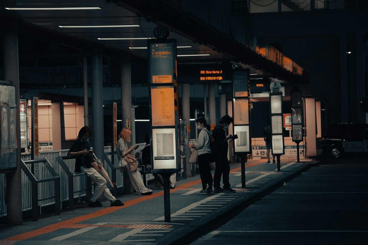 People waiting at a bus stop at night with soft lighting and visible bus schedules