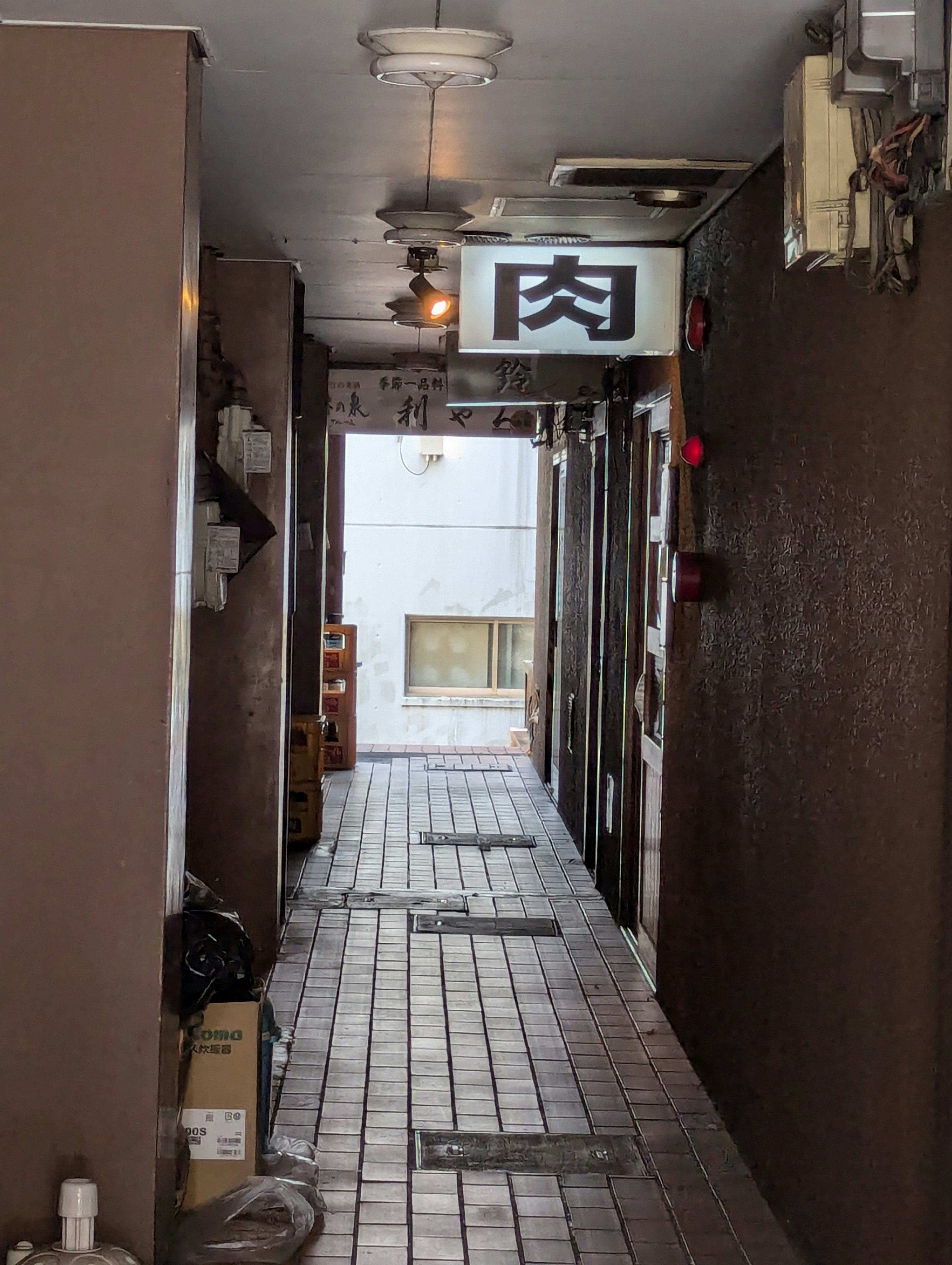 路地の通路に掲げられた「肉」看板のある飲食店の入口