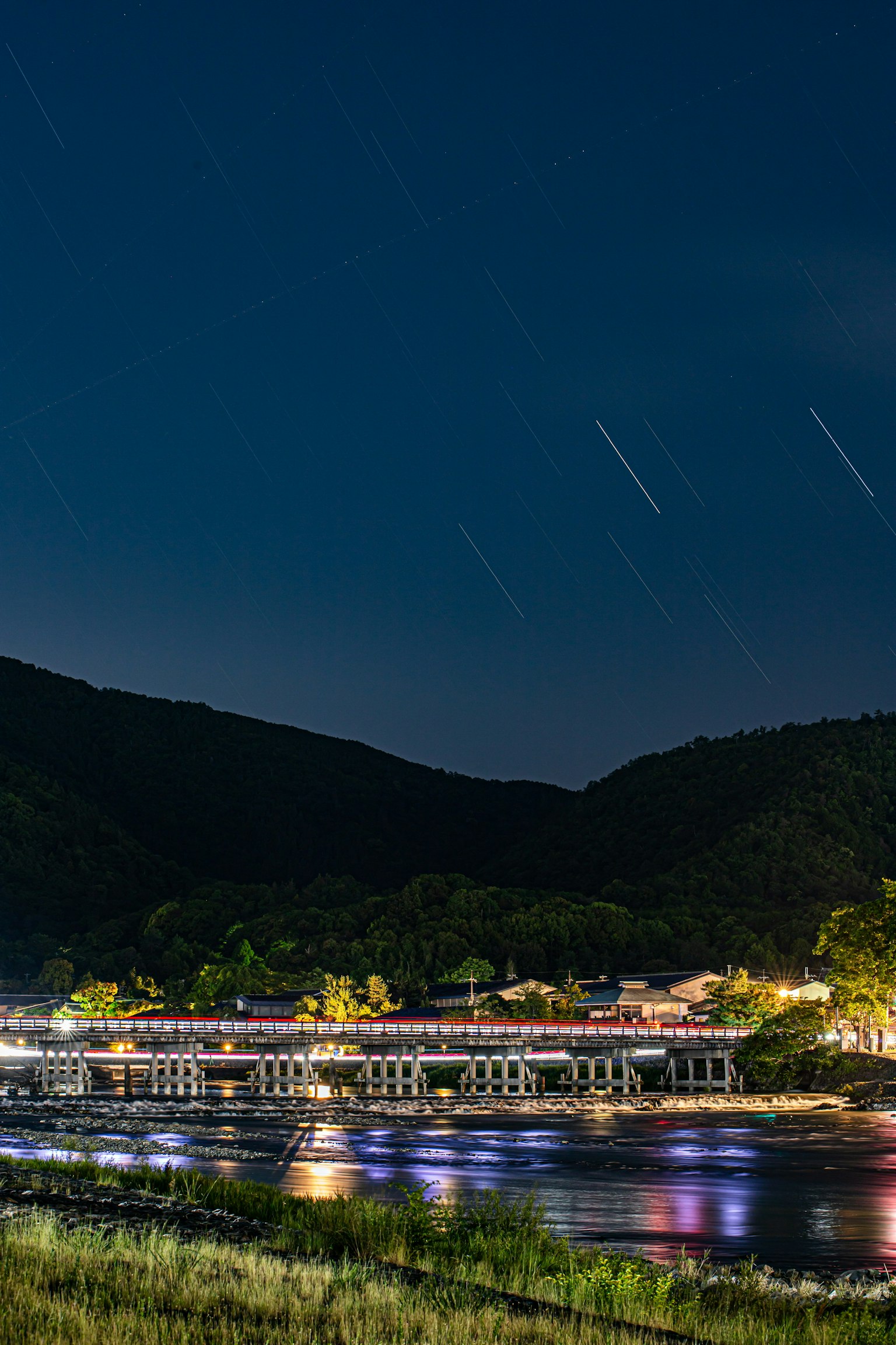 Scène nocturne d'une rivière avec des traînées d'étoiles et un pont illuminé