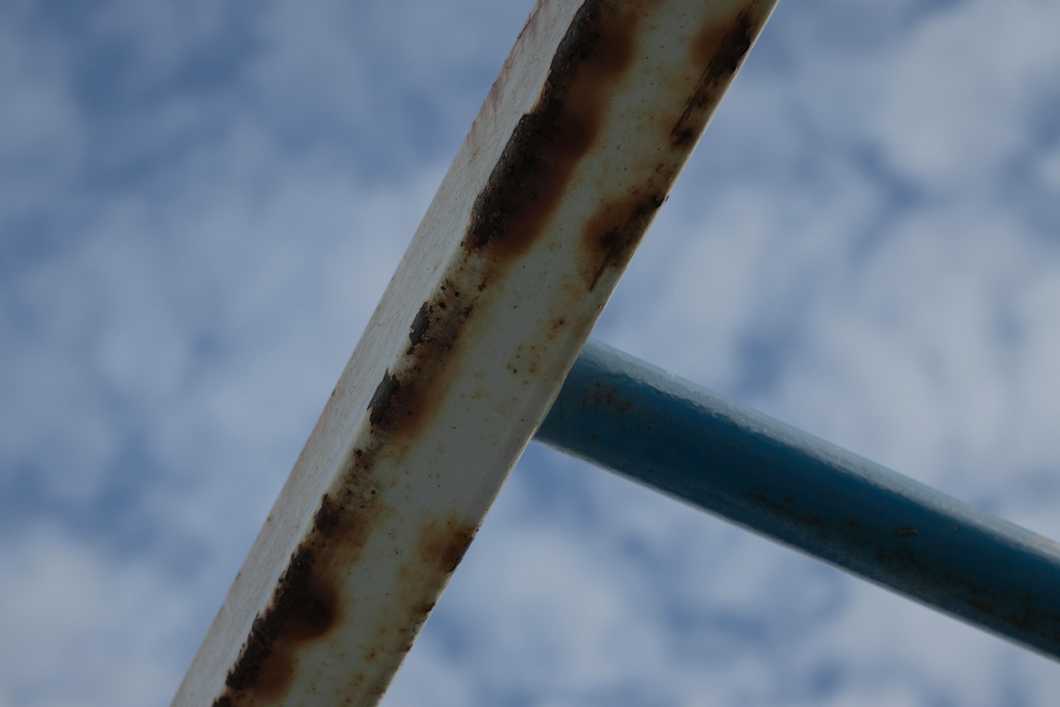Nahaufnahme einer rostigen Metallstange vor einem blauen Himmel mit Wolken