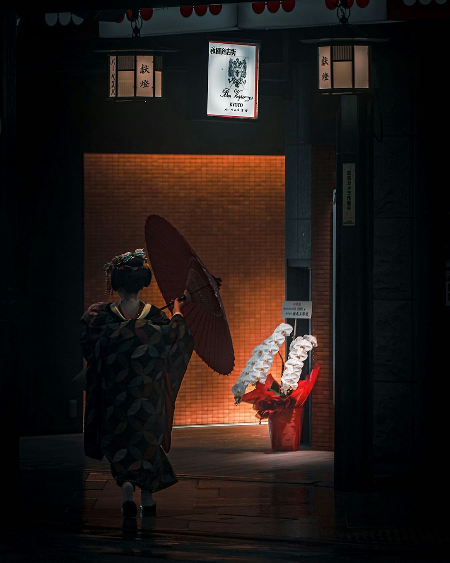 Perempuan dalam kimono tradisional memegang payung merah dengan pintu masuk cerah di latar belakang